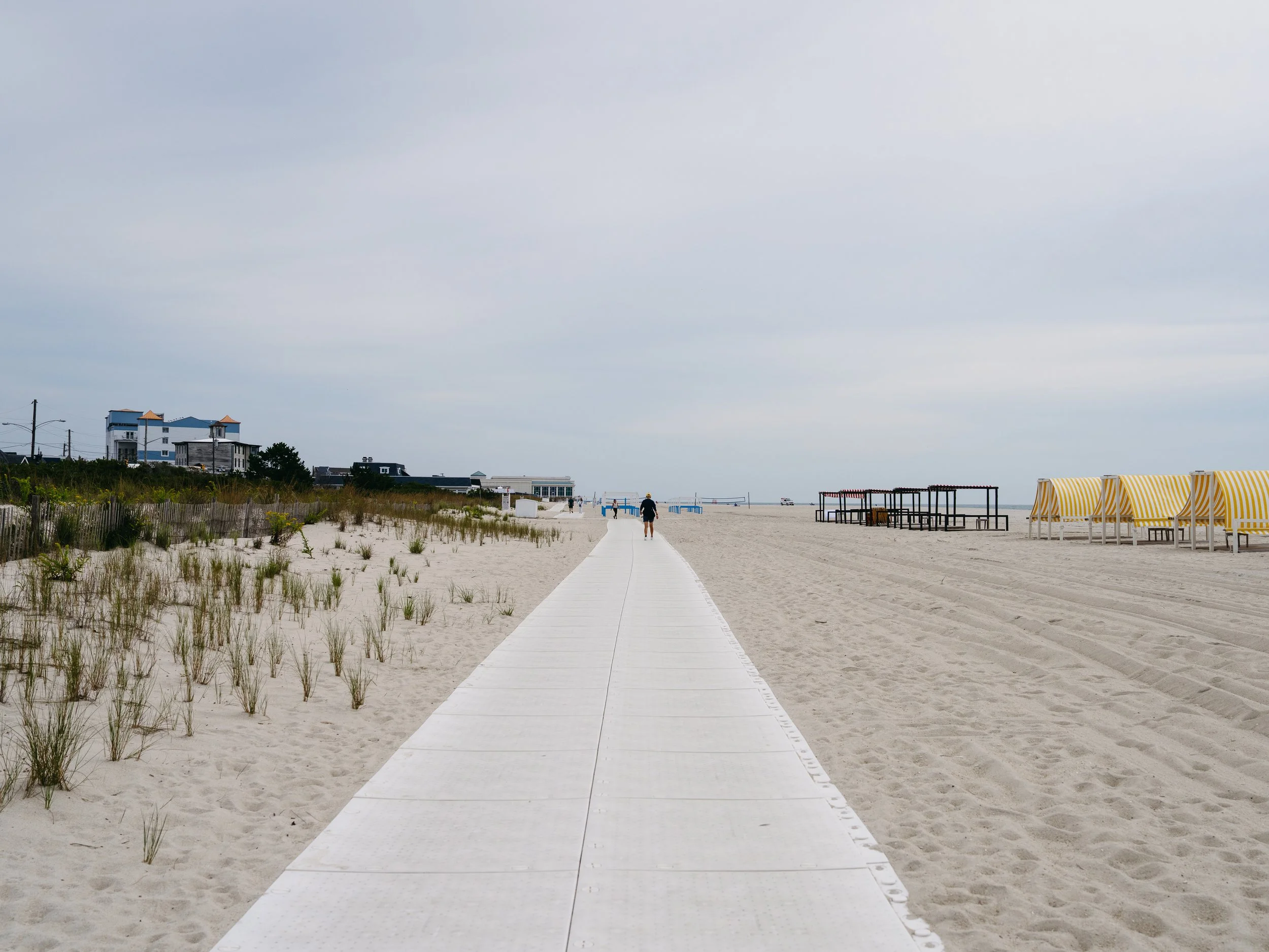 Accessible beach walkway along the dunes at Cape May City Beach, NJ with green dune grass and bright yellow striped cabanas on a sunny summer day