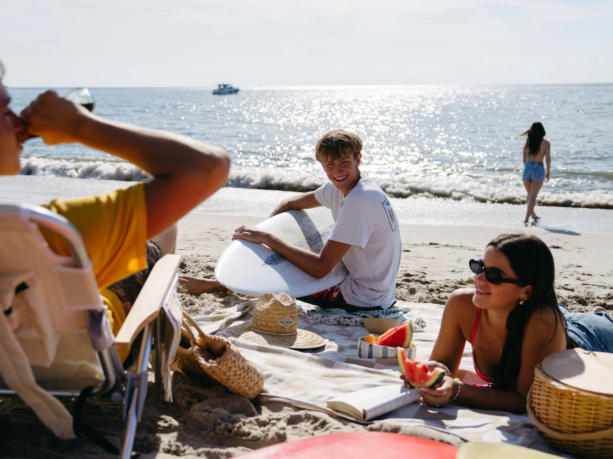 Cape May County, NJ beach day with teens relaxing on a blanket with surfboards and sodas along the Atlantic Ocean on a sunny summer day