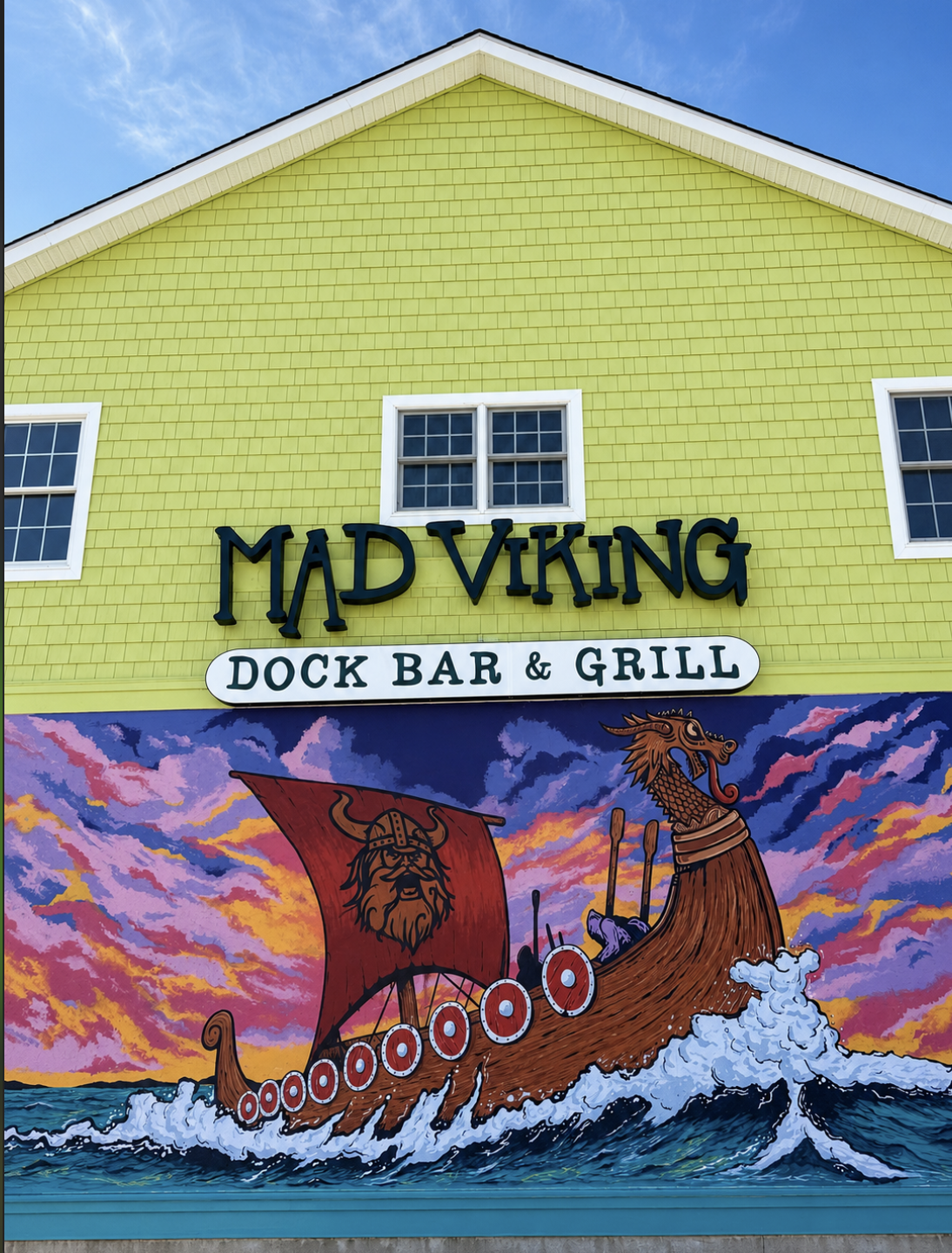 picture of a bright neon green building with a brightly colored themed viking mural with lots of reds and browns. this building the Mad Viking Dock Bar & Grill The Chillest Drinks on Cape May Harbor