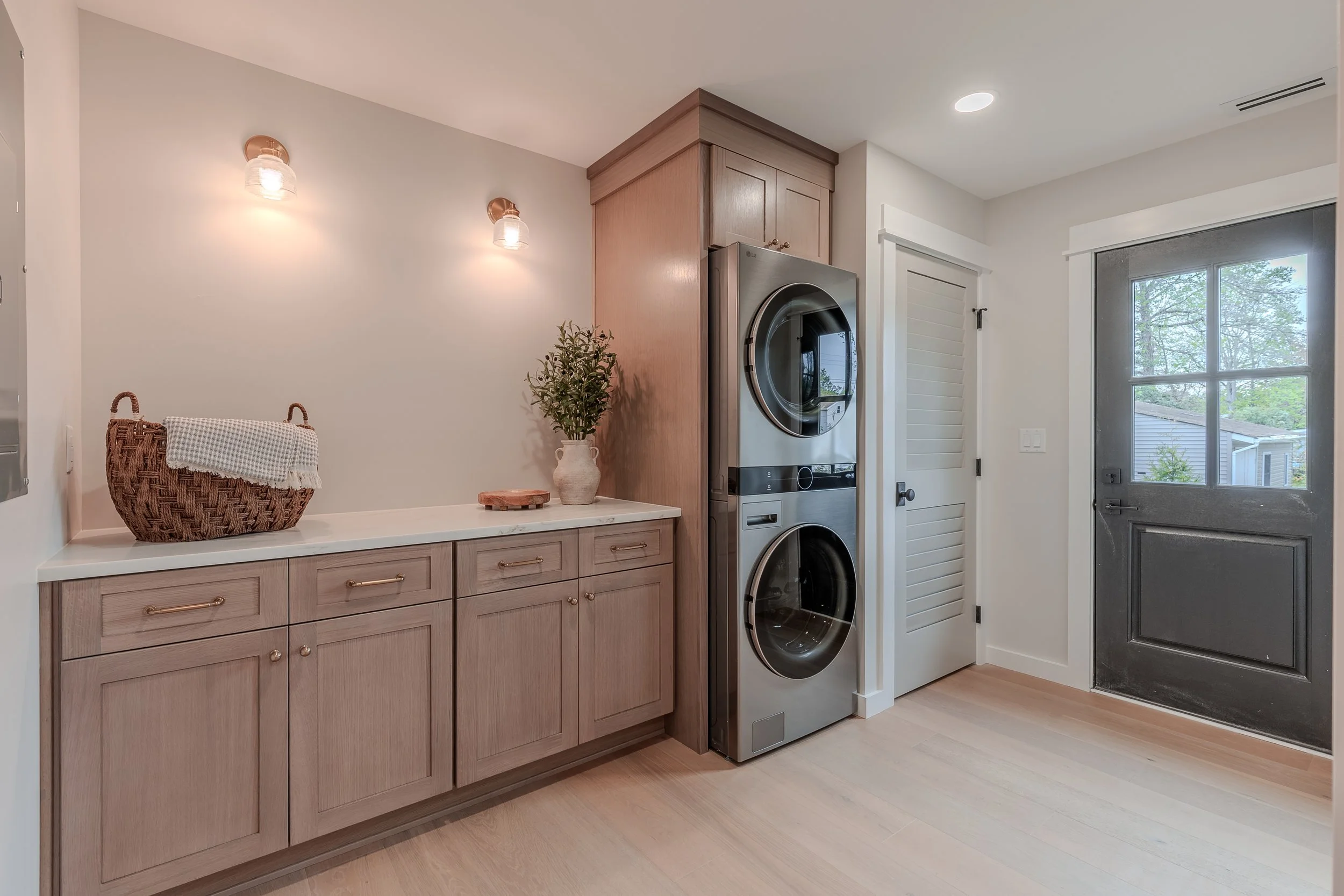 stunning laundry room with stacked double washer dryer, beautiful cabinetry for organization and a side door to the back yard.