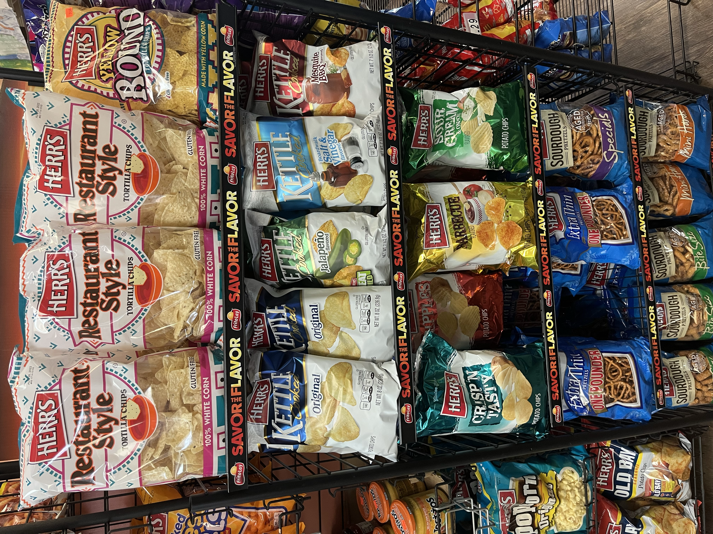Shelves stocked with various bags of Herr's snack chips, including White Corn Tortilla Chips, Flavored Potato Chips, and Pretzels.