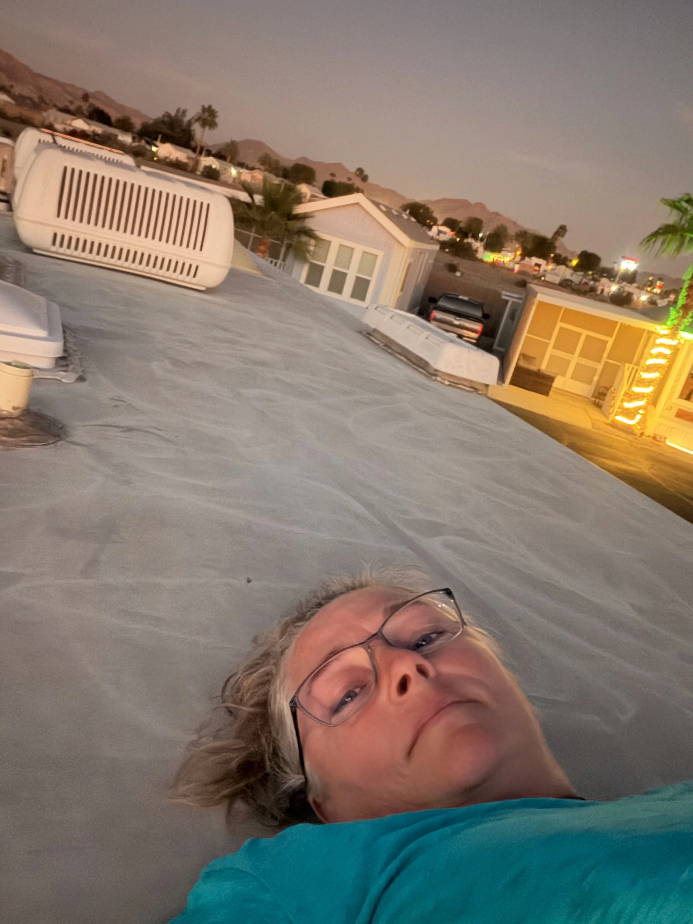A photo of me laying down on the top of our RV with the neighboring park models in the background. The foothills are far off in the distance standing out against the twilight sky.