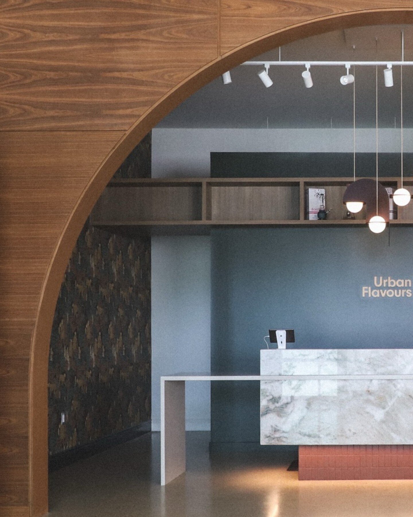 The reception counter at Urban Flavours reads like a concierge desk with a custom teak arched threshold, which allowed for an intimate micro environment &ndash; a room-within-a-room feel. ⁠
⁠
The desk features Venaria Reale stone from Prairie Stone M