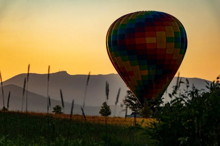 A hot air balloon lands as the sun sets behind Mount Mansfield