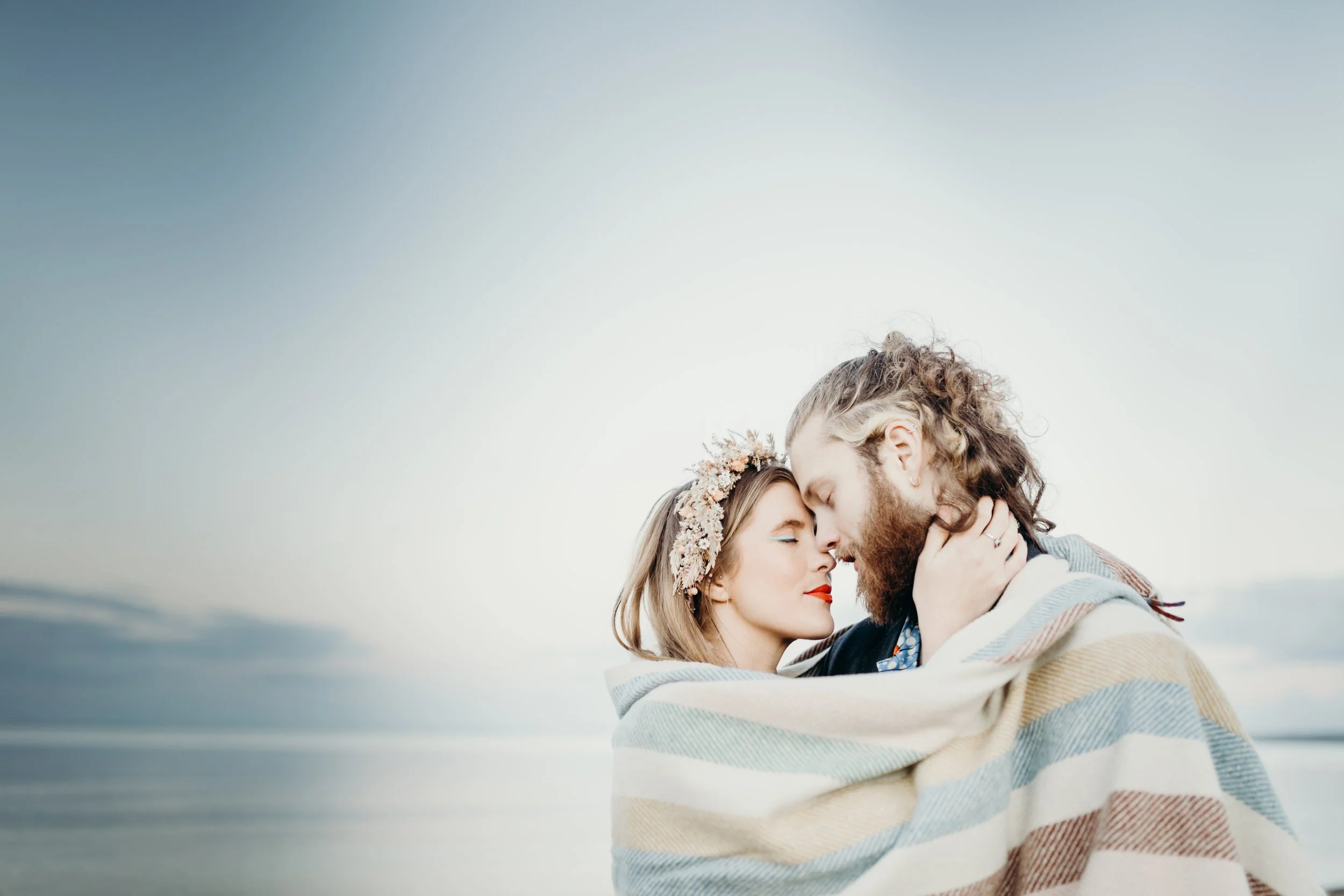A couple with closed eyes and wrapped in a blanket, embracing closely at the beach.