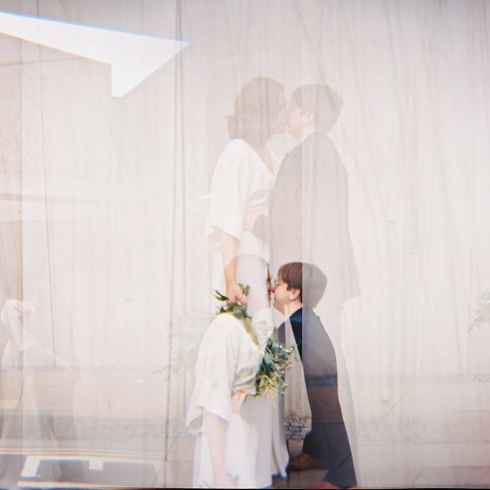 A reflection of a wedding scene showing couple kissing, a woman with a bouquet, and a man in formal attire.
