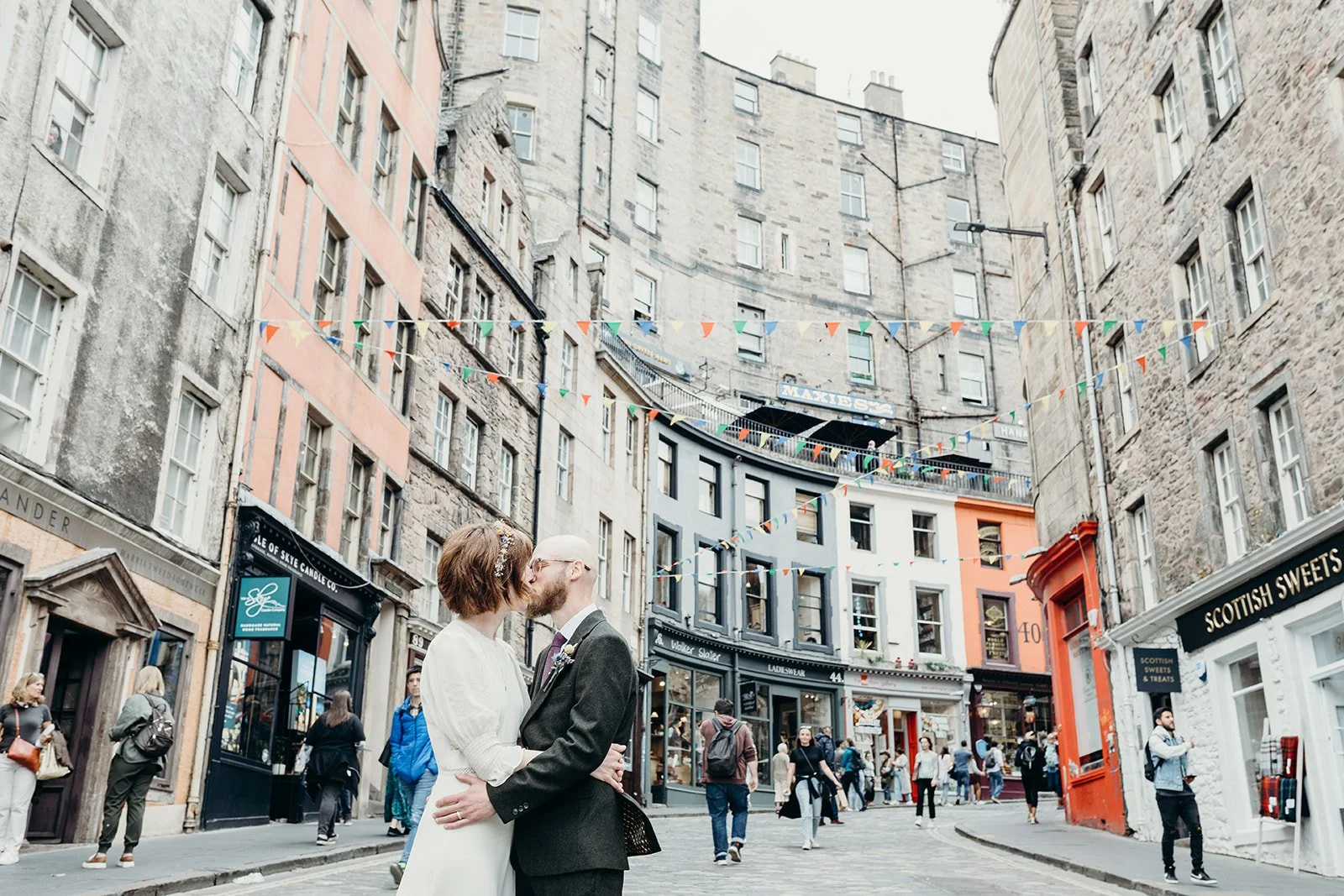 A couple sharing a kiss in the middle of a busy city street with colorful buildings and string decorations overhead.