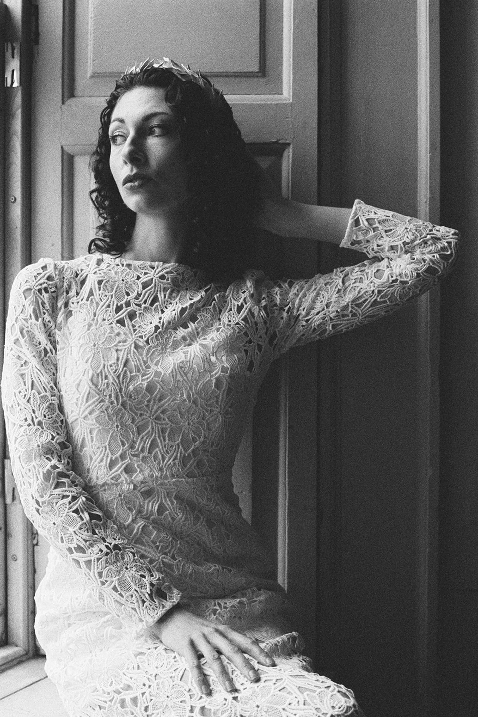 brand photographer shoot .A woman dressed in a lace dress, sitting near a window with her hand resting on her lap, looking away.