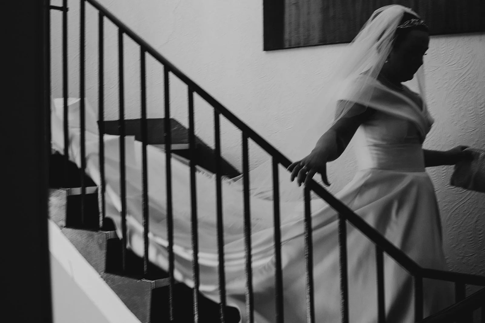 A woman in a wedding dress and veil descending a staircase in black and white.