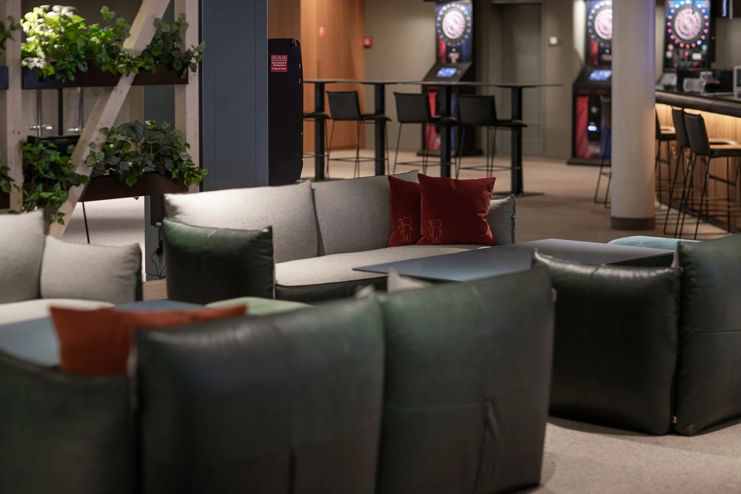 Swiss Holiday Park Sportsbar lounge with dark green and grey seating, accent cushions and darts boards beyond.
