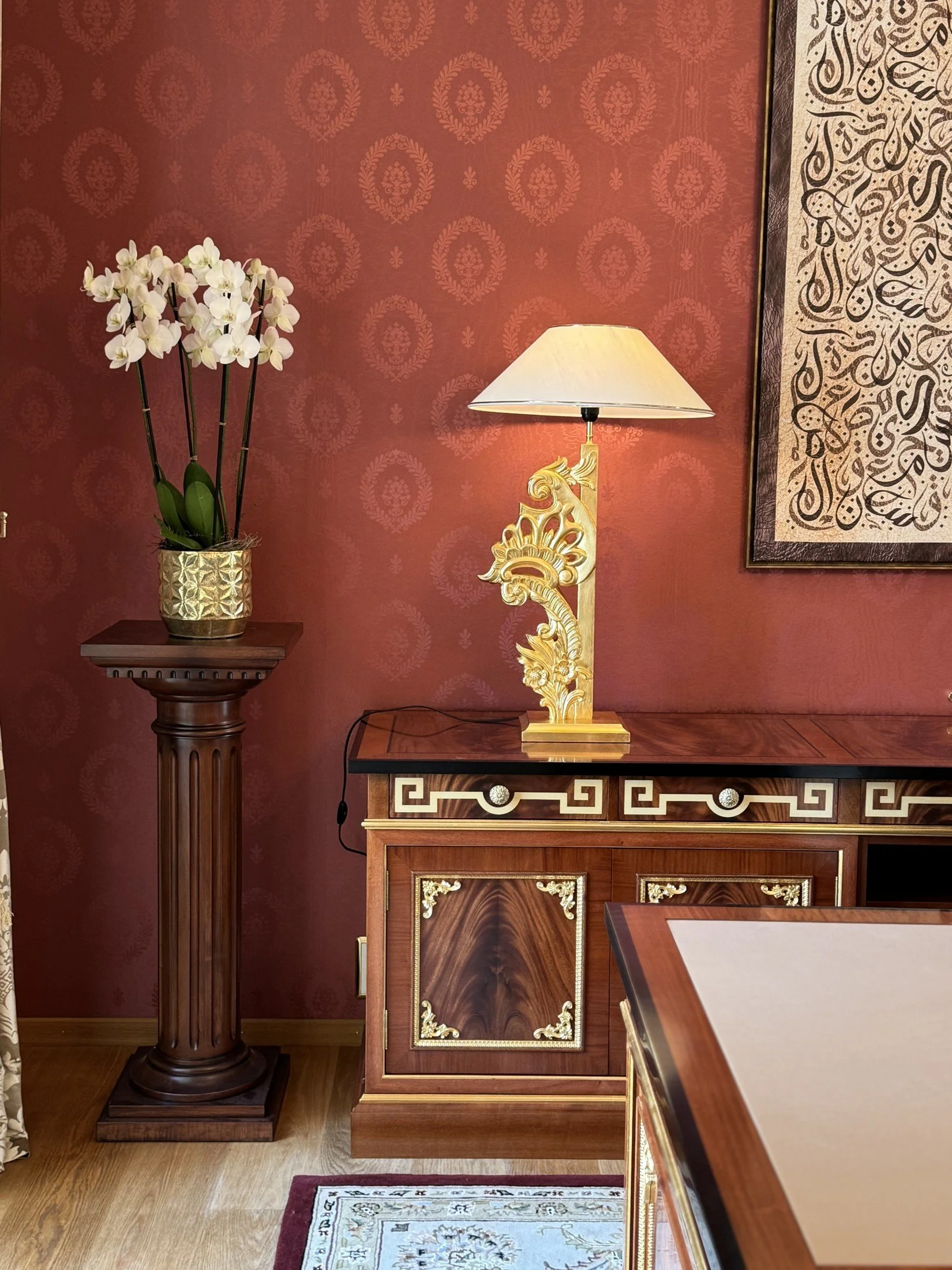Red and gold interior detail with an ornate sideboard and table lamp.