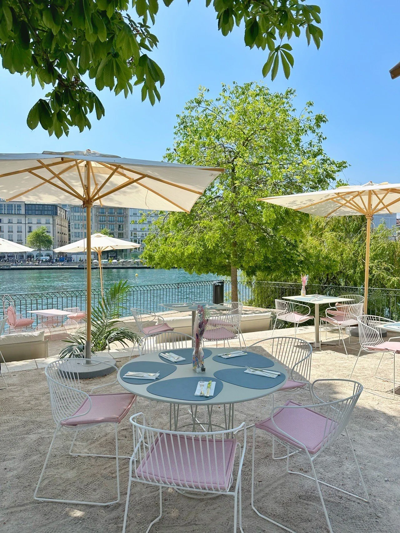 Geneva summer pop-up terrace with pastel chairs, small dining tables and cream parasols beside the water.