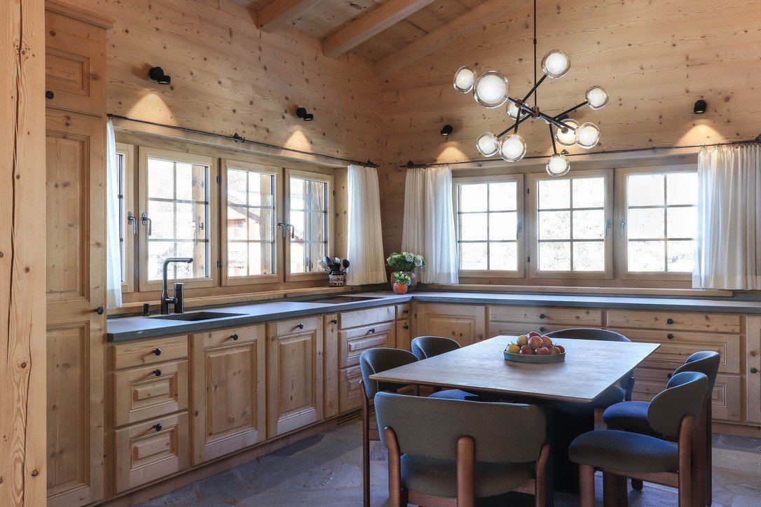 Alpine apartment kitchen and dining area beneath an exposed timber ceiling.
