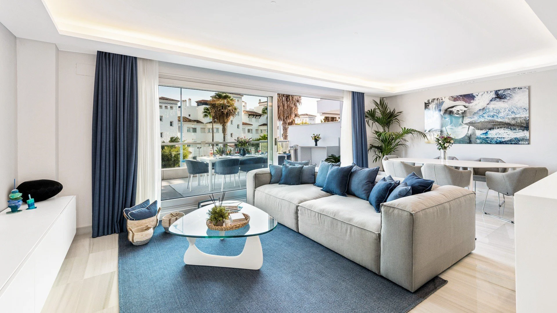 Marbella holiday home living room with pale sofas, blue textiles and broad windows towards the terrace.