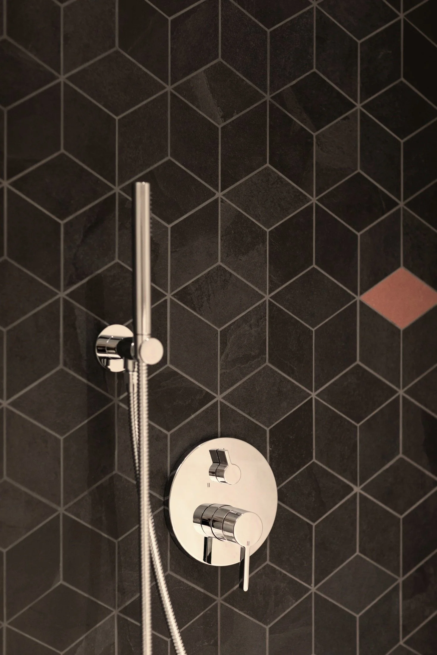 Bathroom shower detail with dark geometric tiles and chrome fixtures.