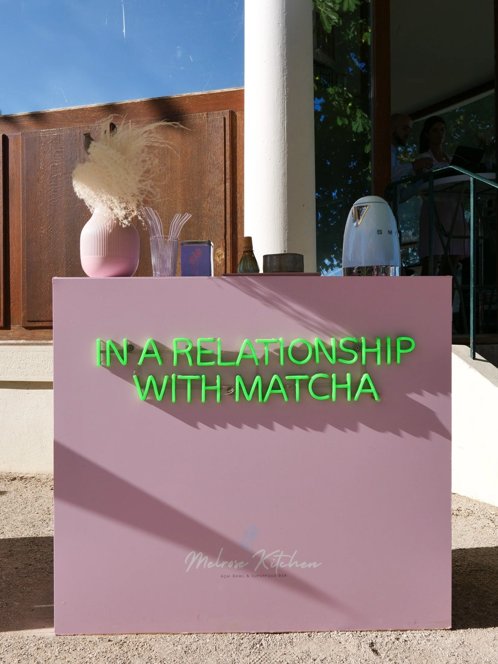 Pink pop-up bar counter with green lettering and a relaxed outdoor setting.