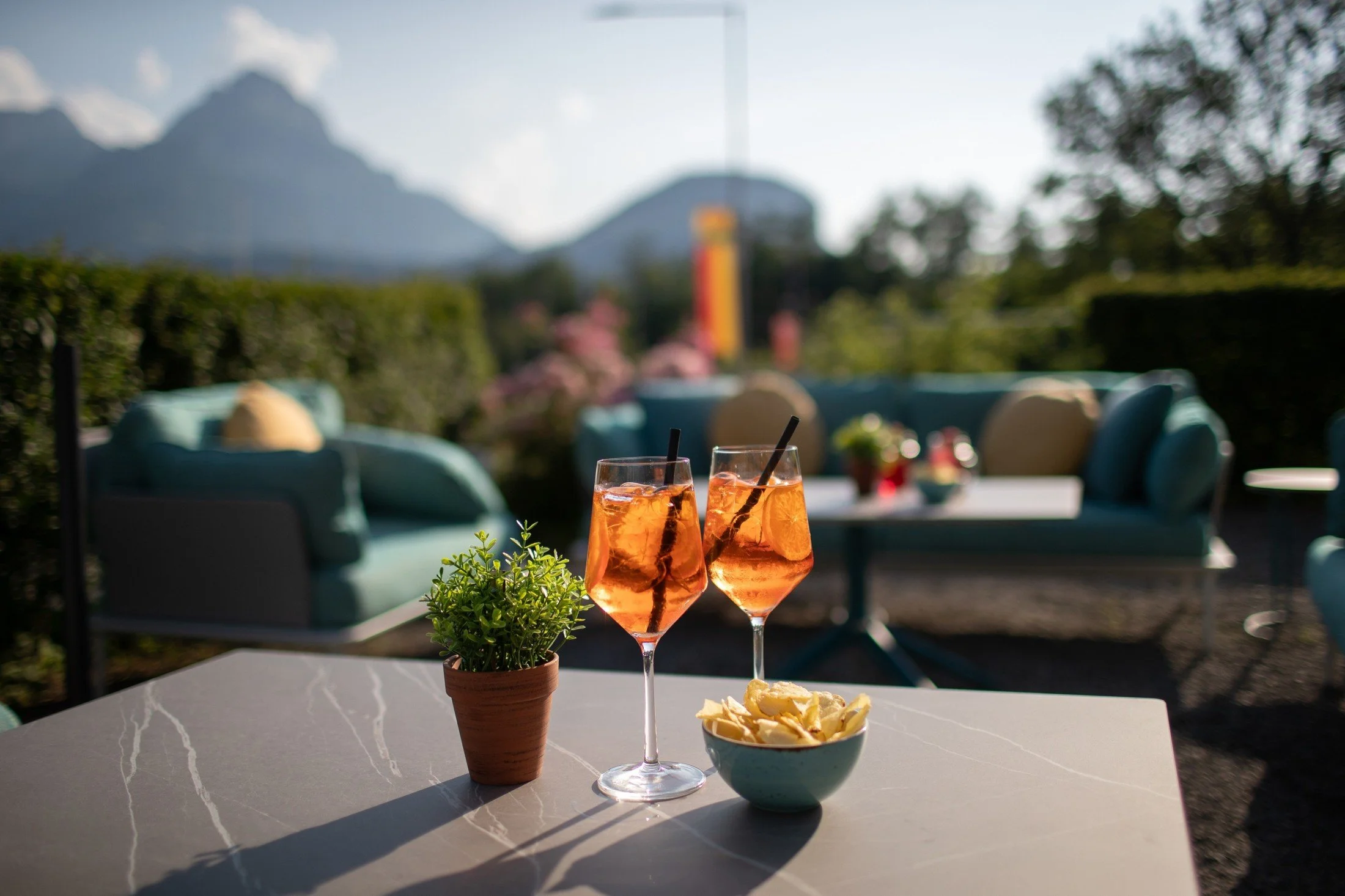 Drinks and snacks on a Siam Restaurant terrace table, with lounge seating and Alpine scenery beyond.