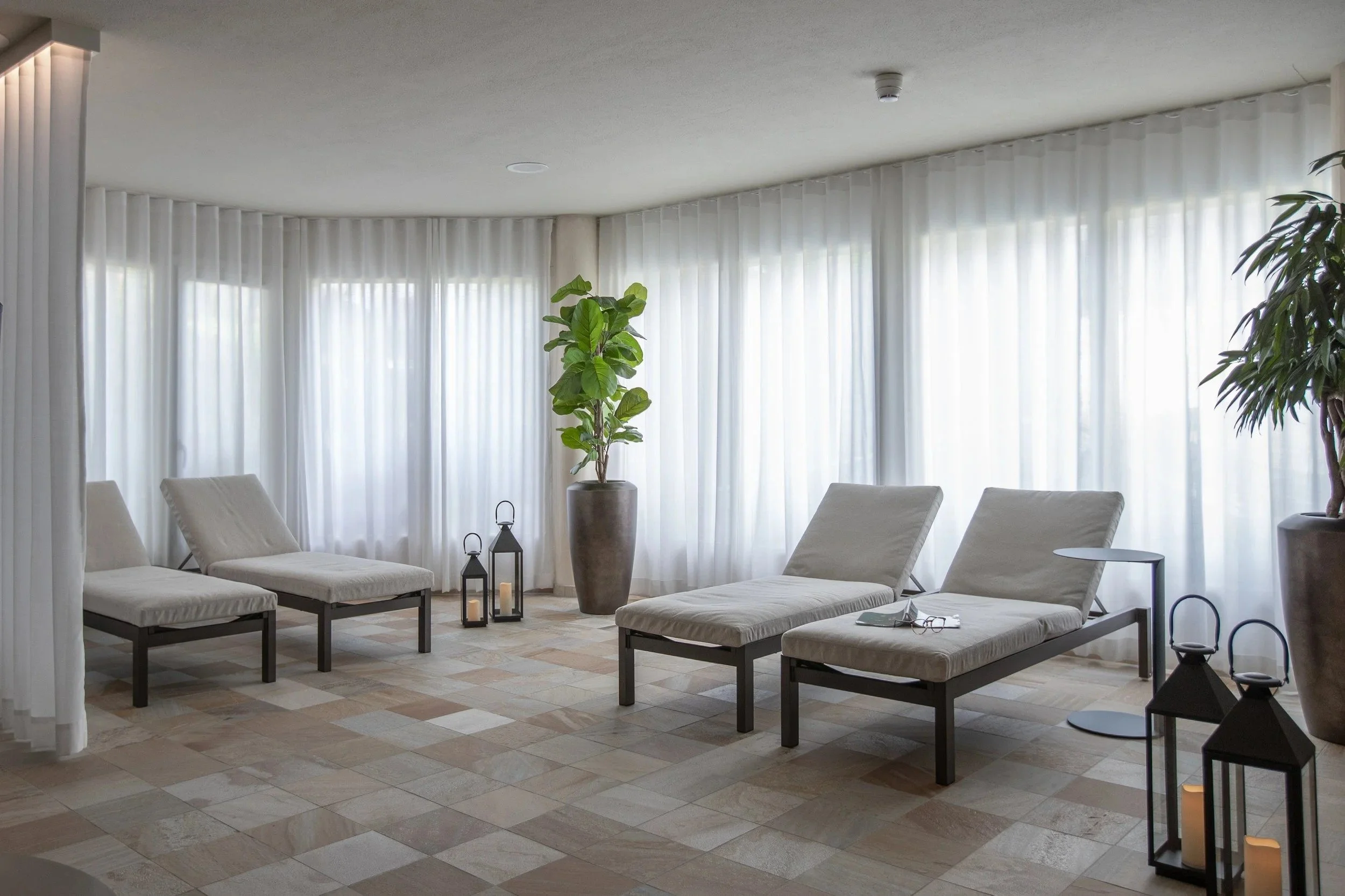 Swiss Holiday Park spa relaxation room with padded loungers, sheer curtains, plants and lanterns.