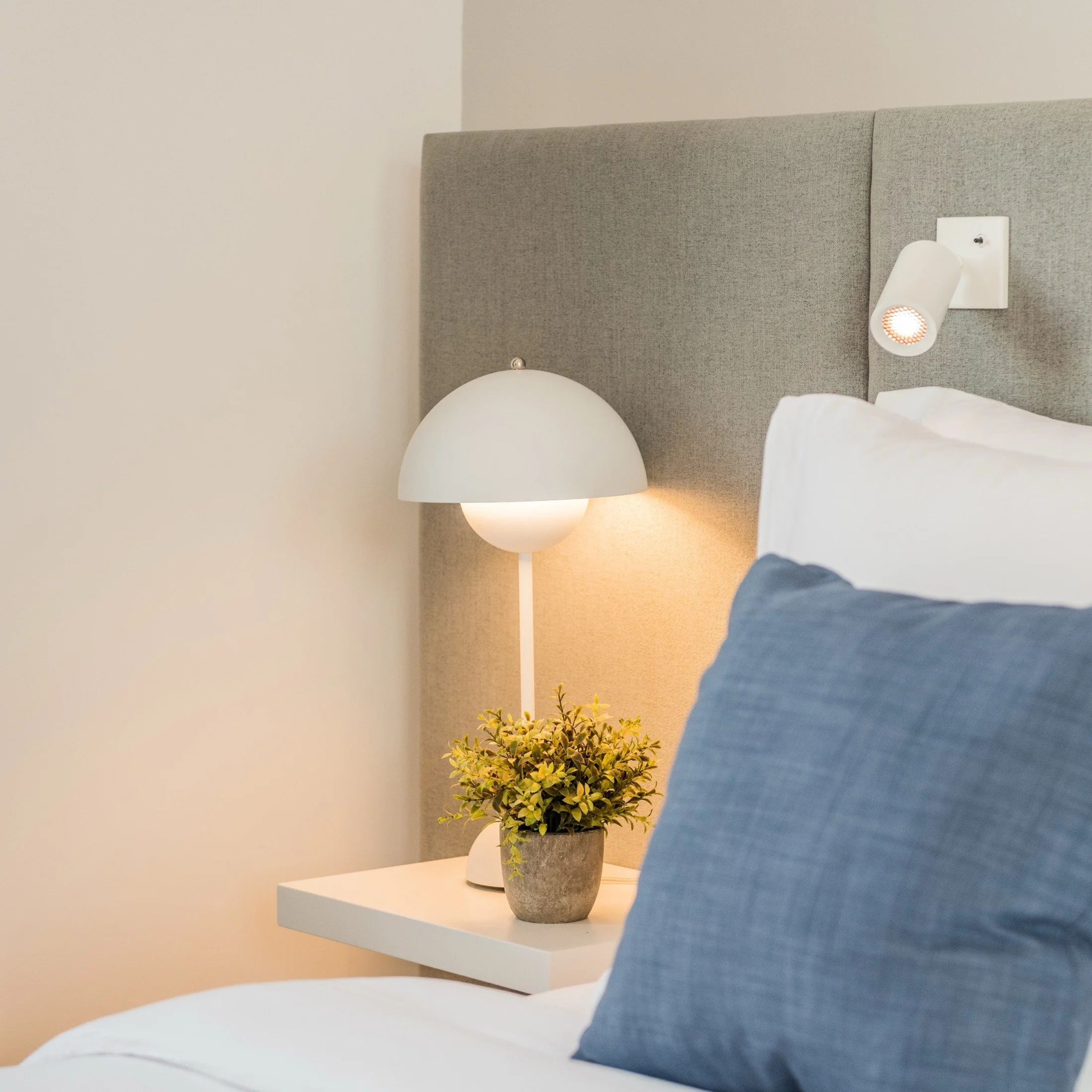 Bedroom detail with a round bedside lamp and blue cushion against neutral upholstery.