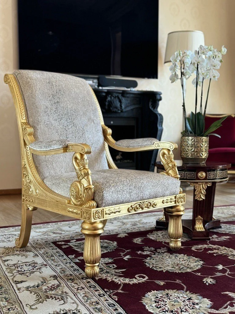 Gilded armchair beside a dark cabinet and decorative accessories.