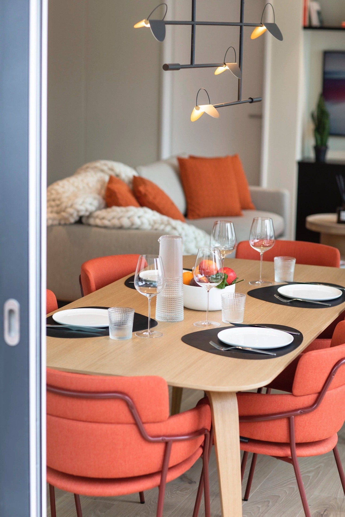 Dining table setting with orange upholstered chairs beside the living area.