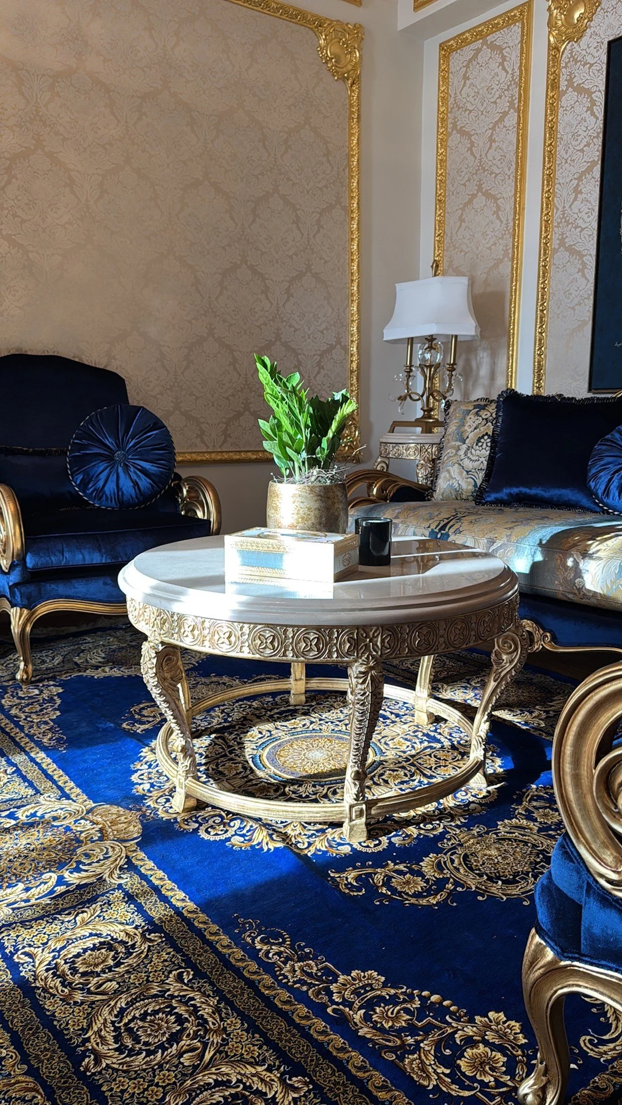 Classic residence seating area with blue upholstery, gilded furniture and a round coffee table.