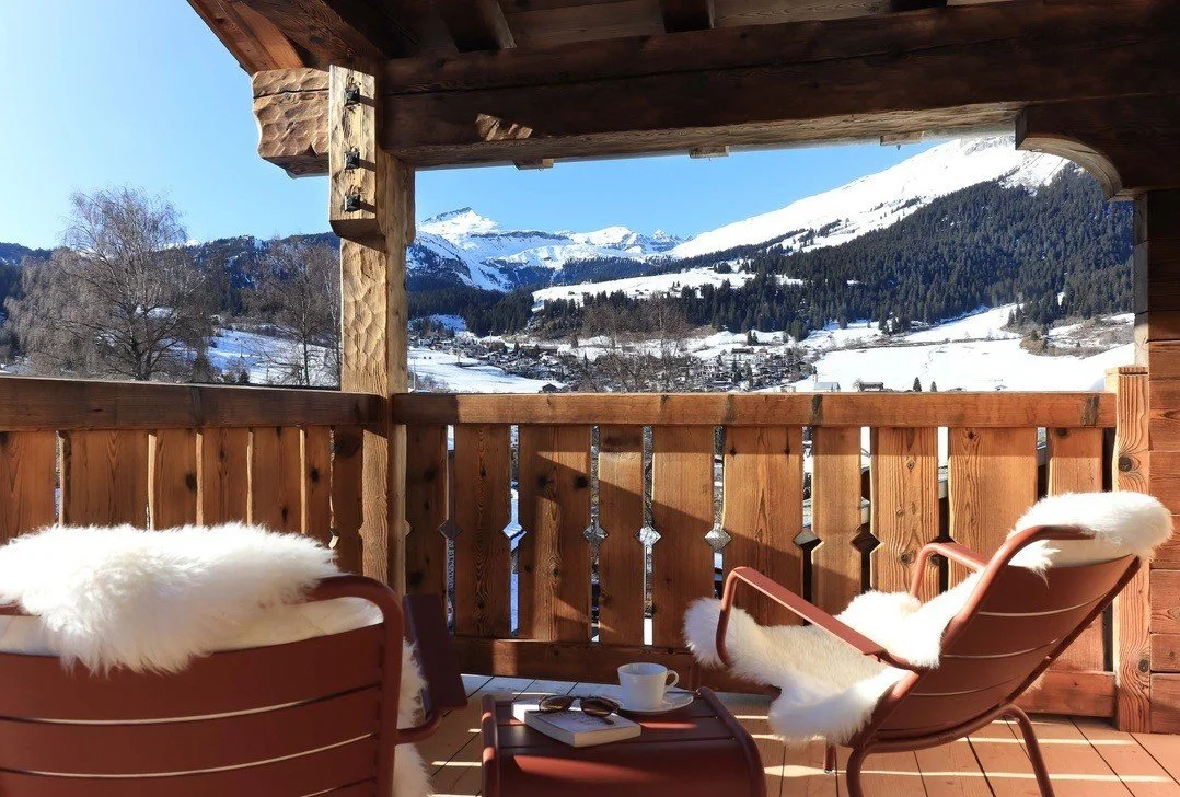 Alpine apartment balcony with timber detailing, lounge chairs and views across a snowy mountain landscape.