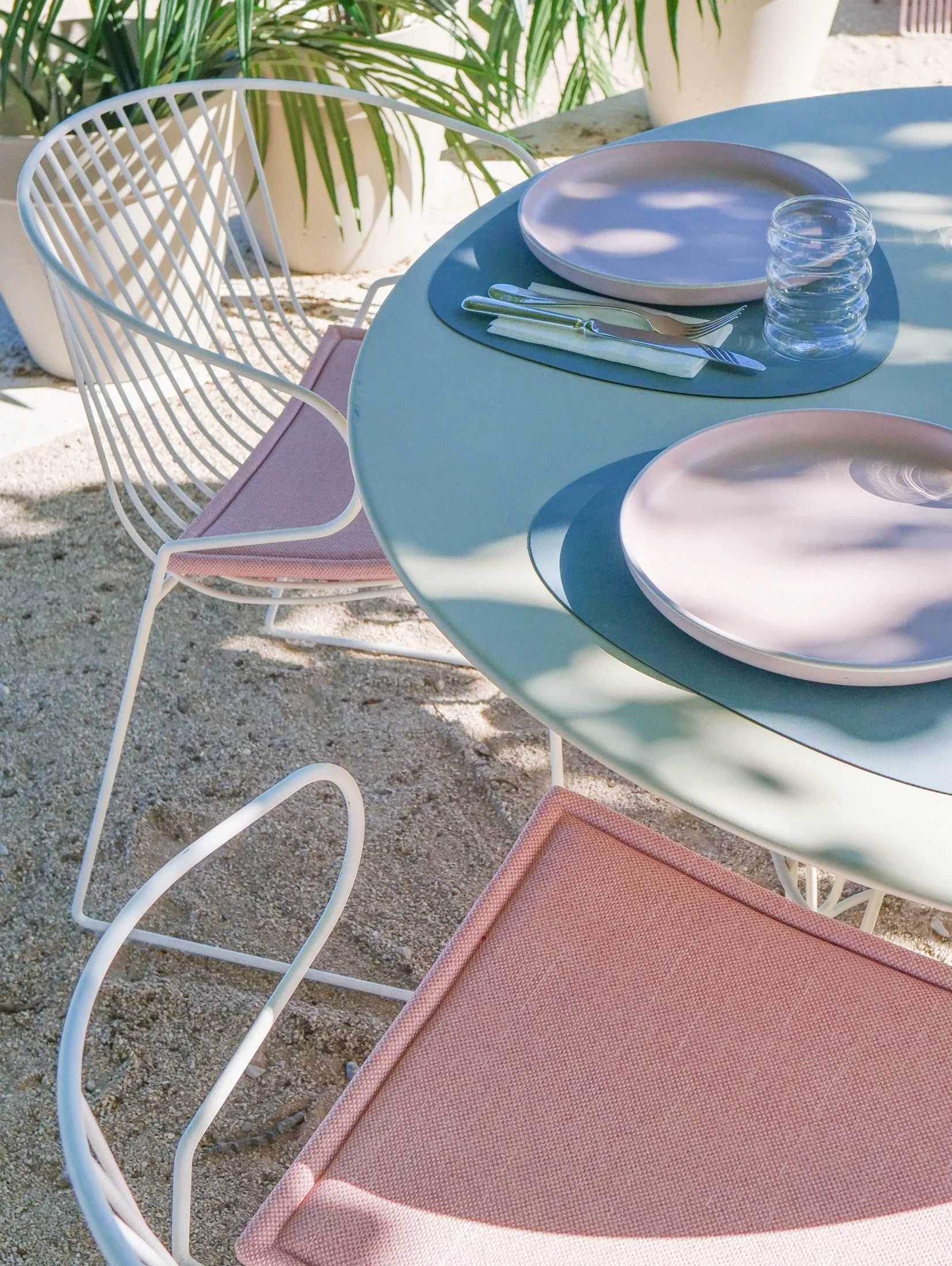 Outdoor table setting with pastel plates, coloured glassware and woven seating.