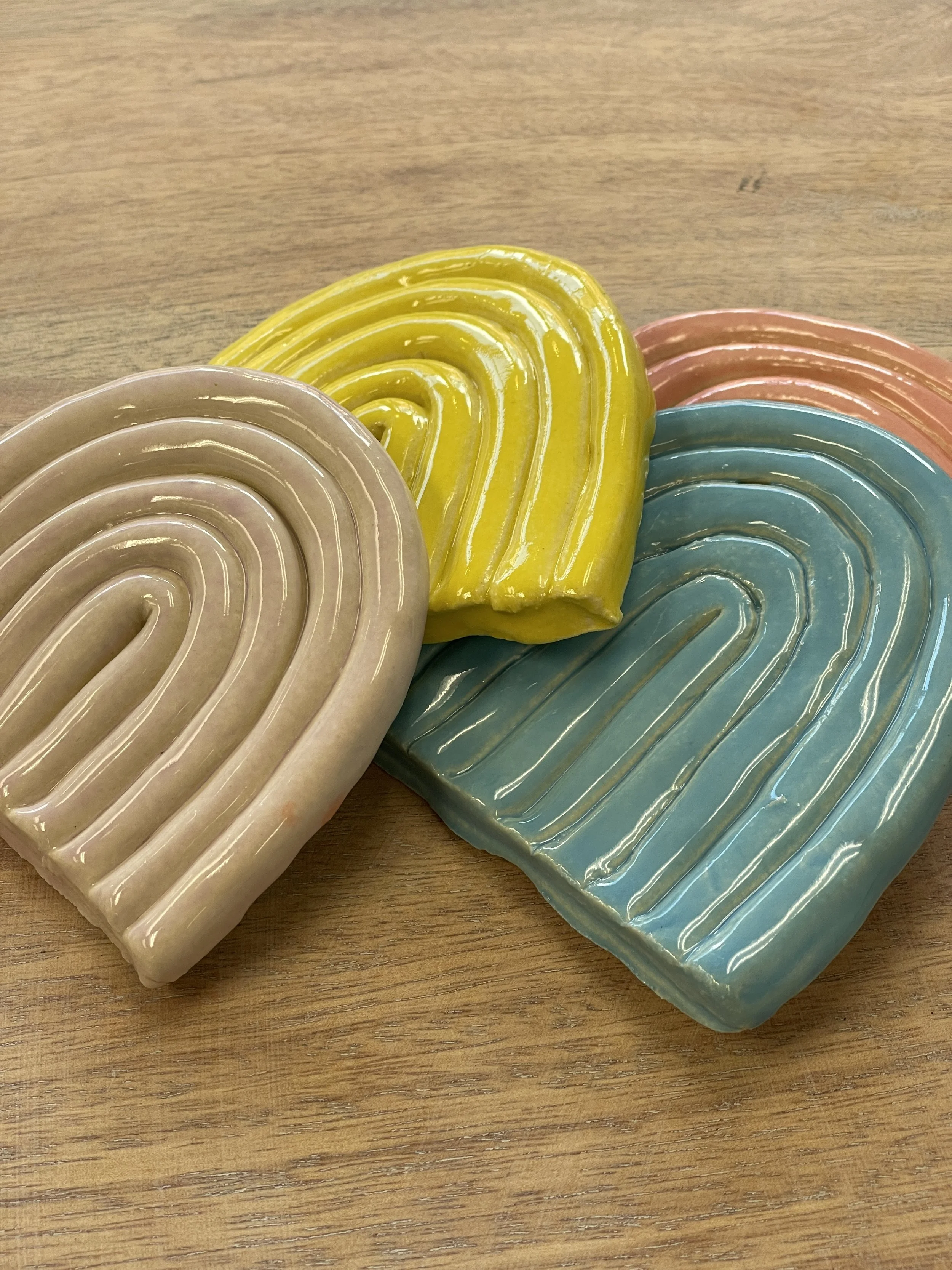 Colorful ceramic coasters with abstract rainbow patterns on a wooden surface.