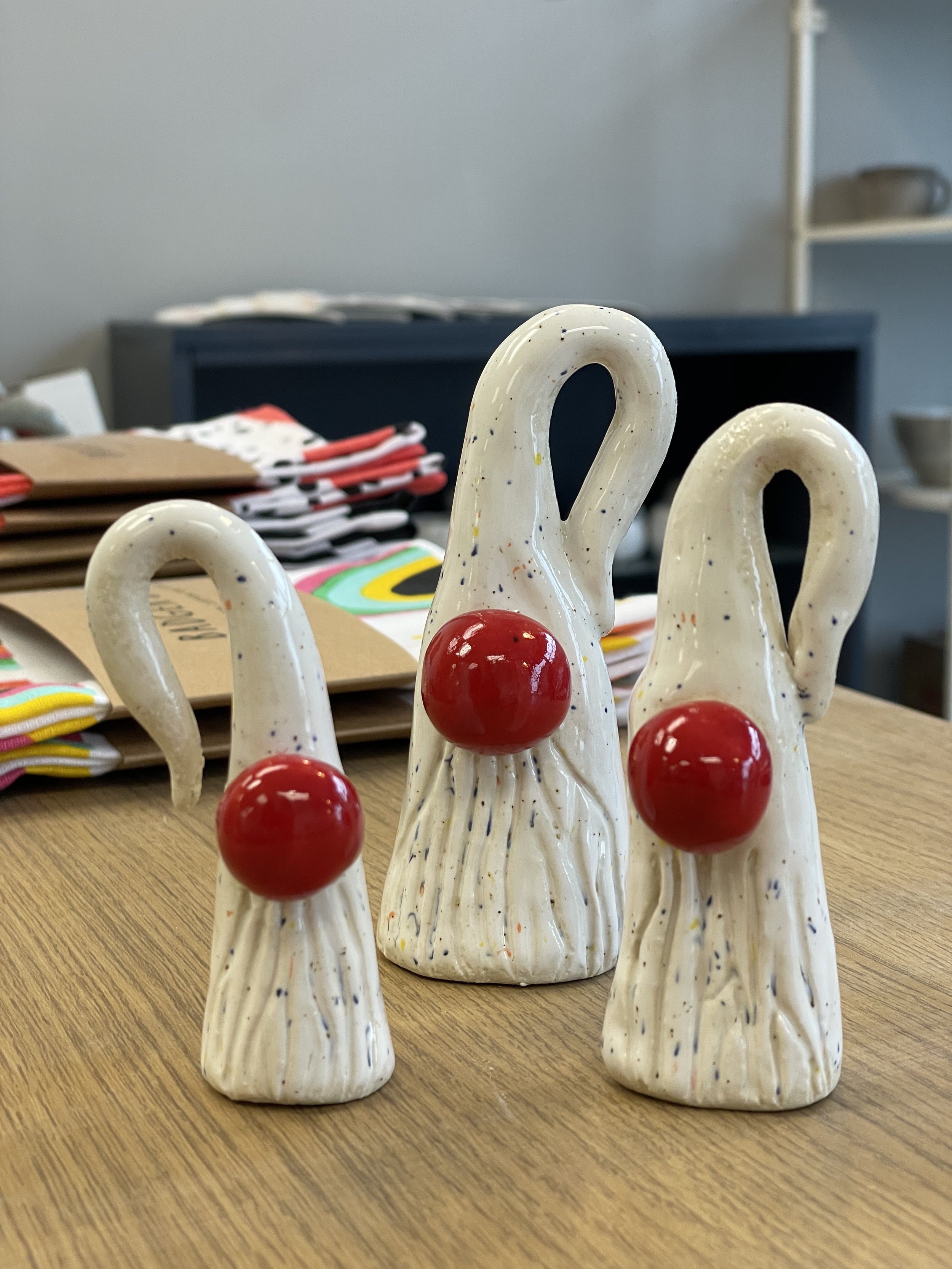 Three ceramic gnome-like figures with white speckled bodies and prominent red noses on a wooden table.