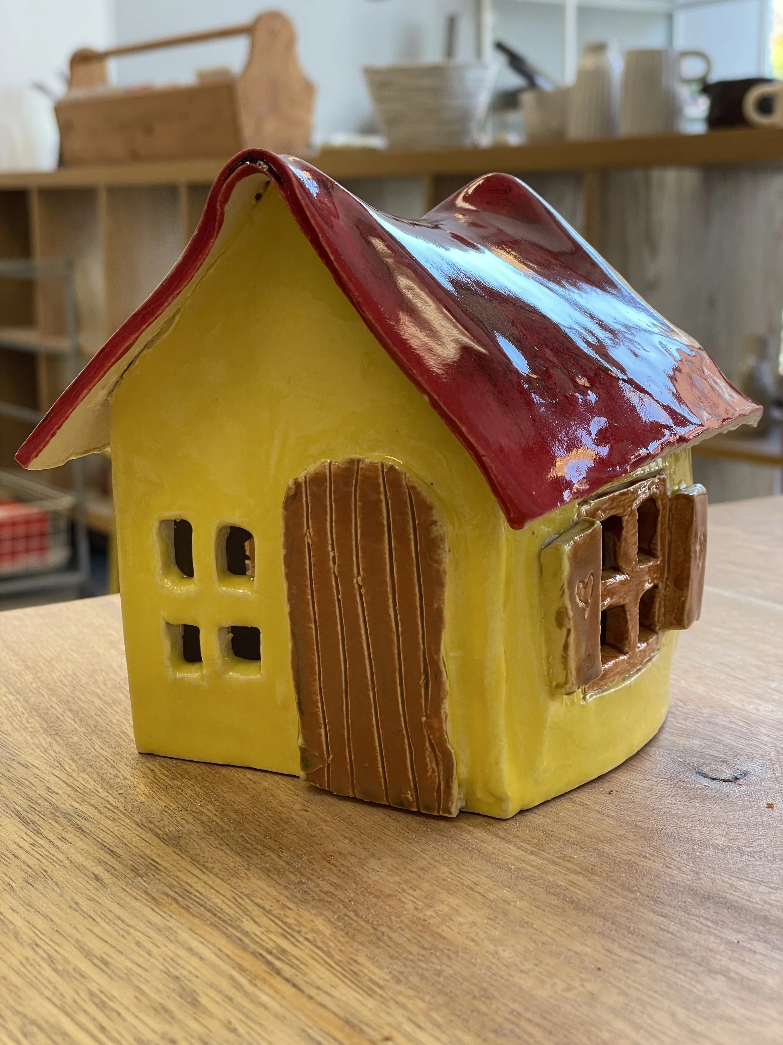 Ceramic mini house with yellow walls and red roof on a wooden table