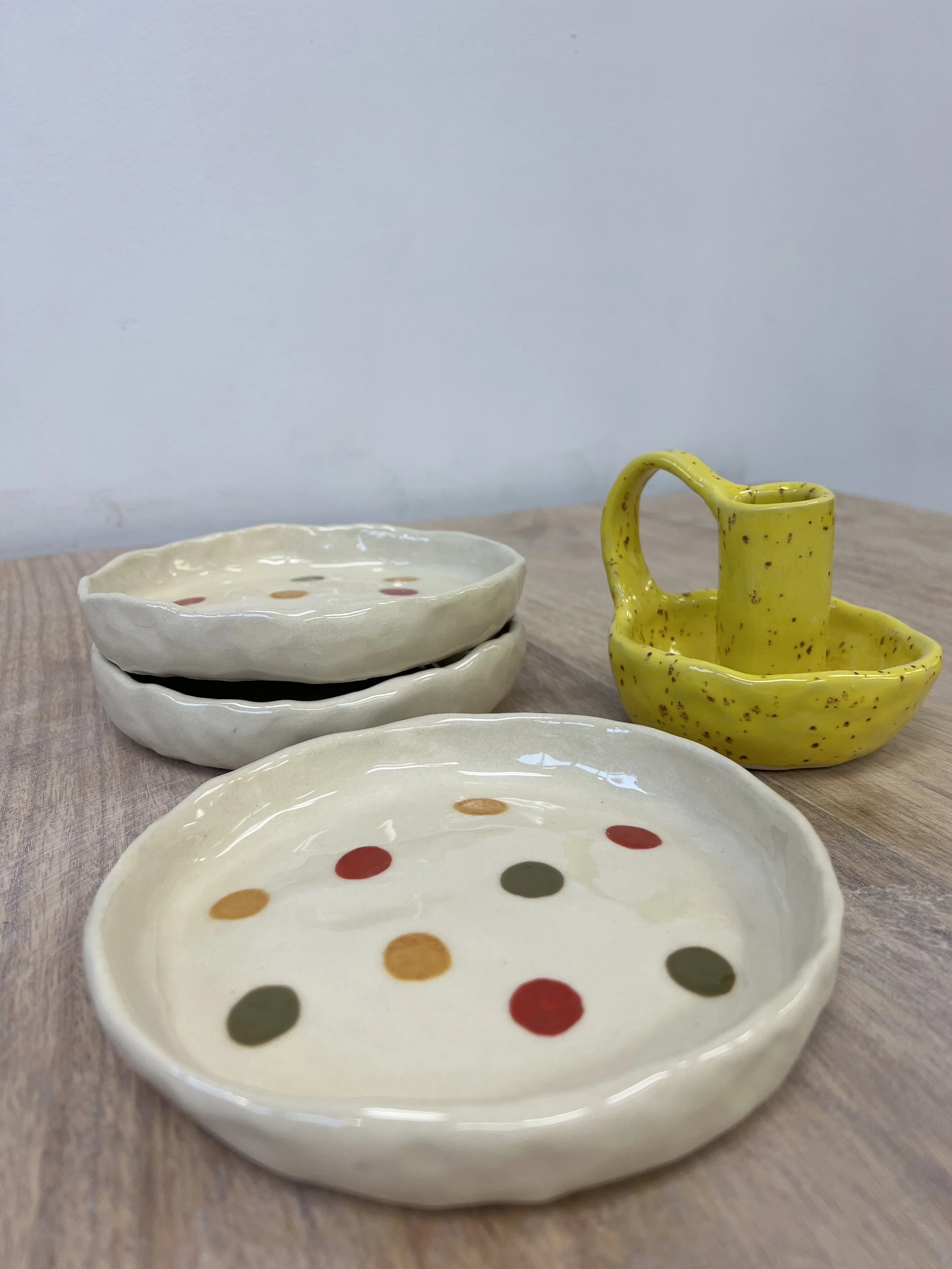 Ceramic plates with polka dot patterns and a small yellow pitcher on a wooden surface.