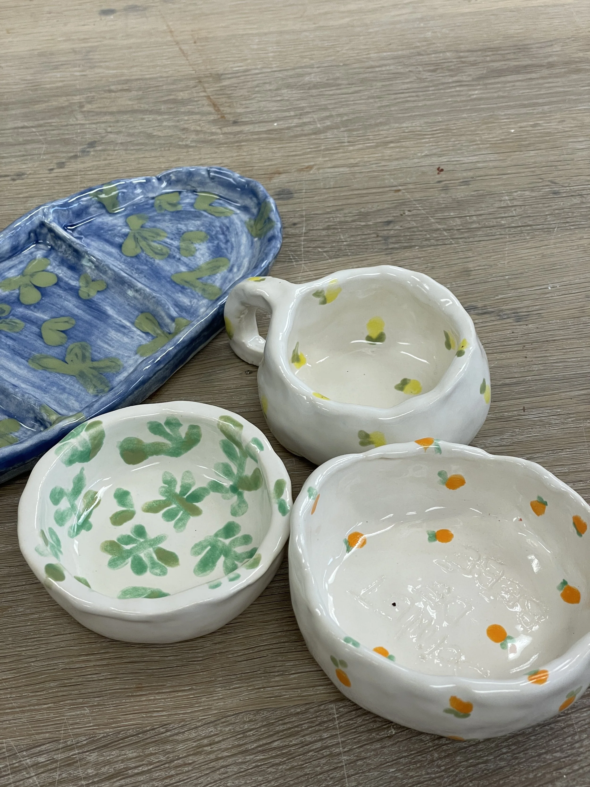 Handmade ceramic dishes with colorful floral patterns on a wooden table.