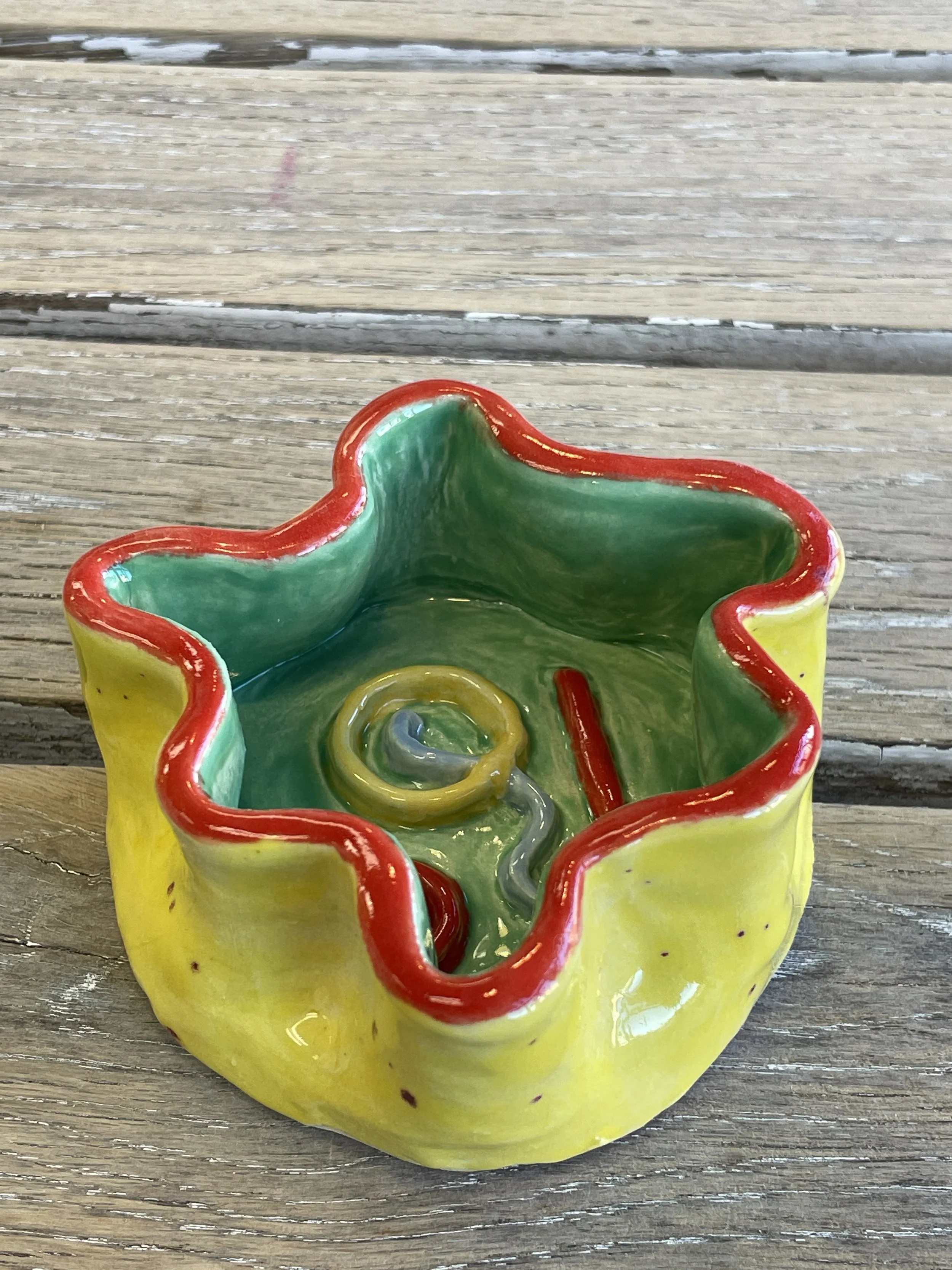 Colorful ceramic dish with wavy edges, featuring a yellow exterior, green interior, and red rim.