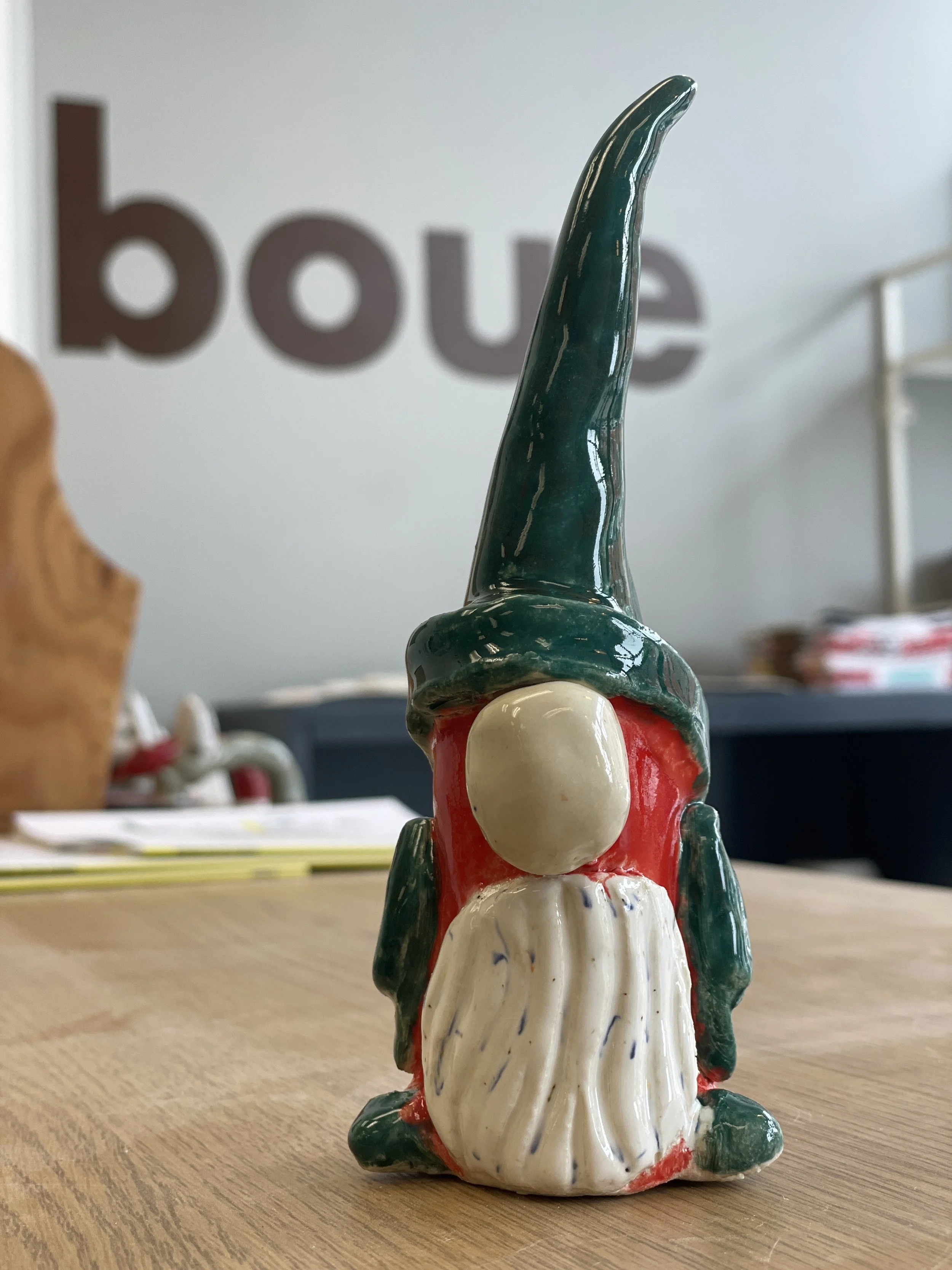 Ceramic gnome figurine with green hat and red body on wooden table.