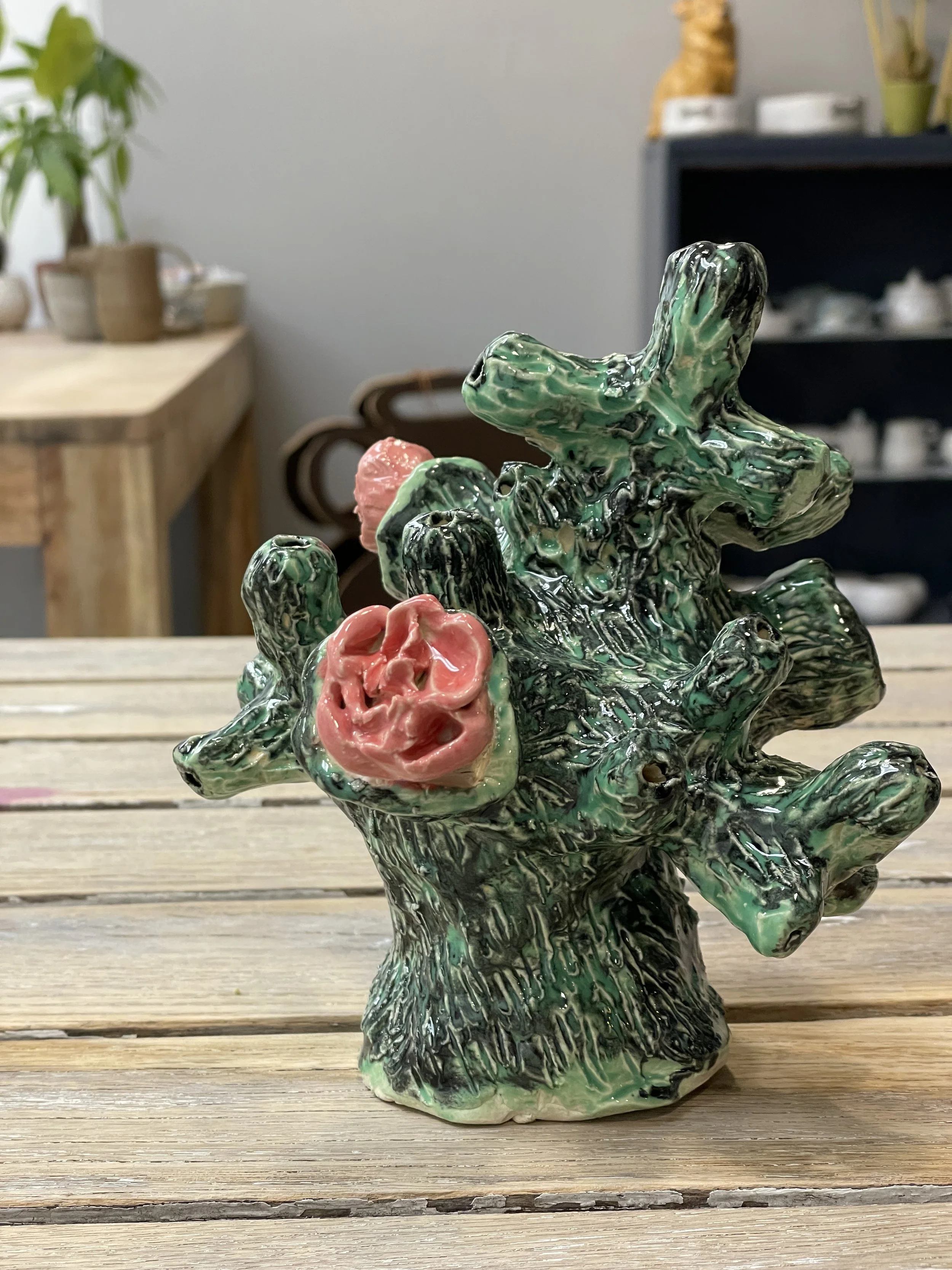 Ceramic sculpture resembling coral with pink and green hues on a wooden surface.