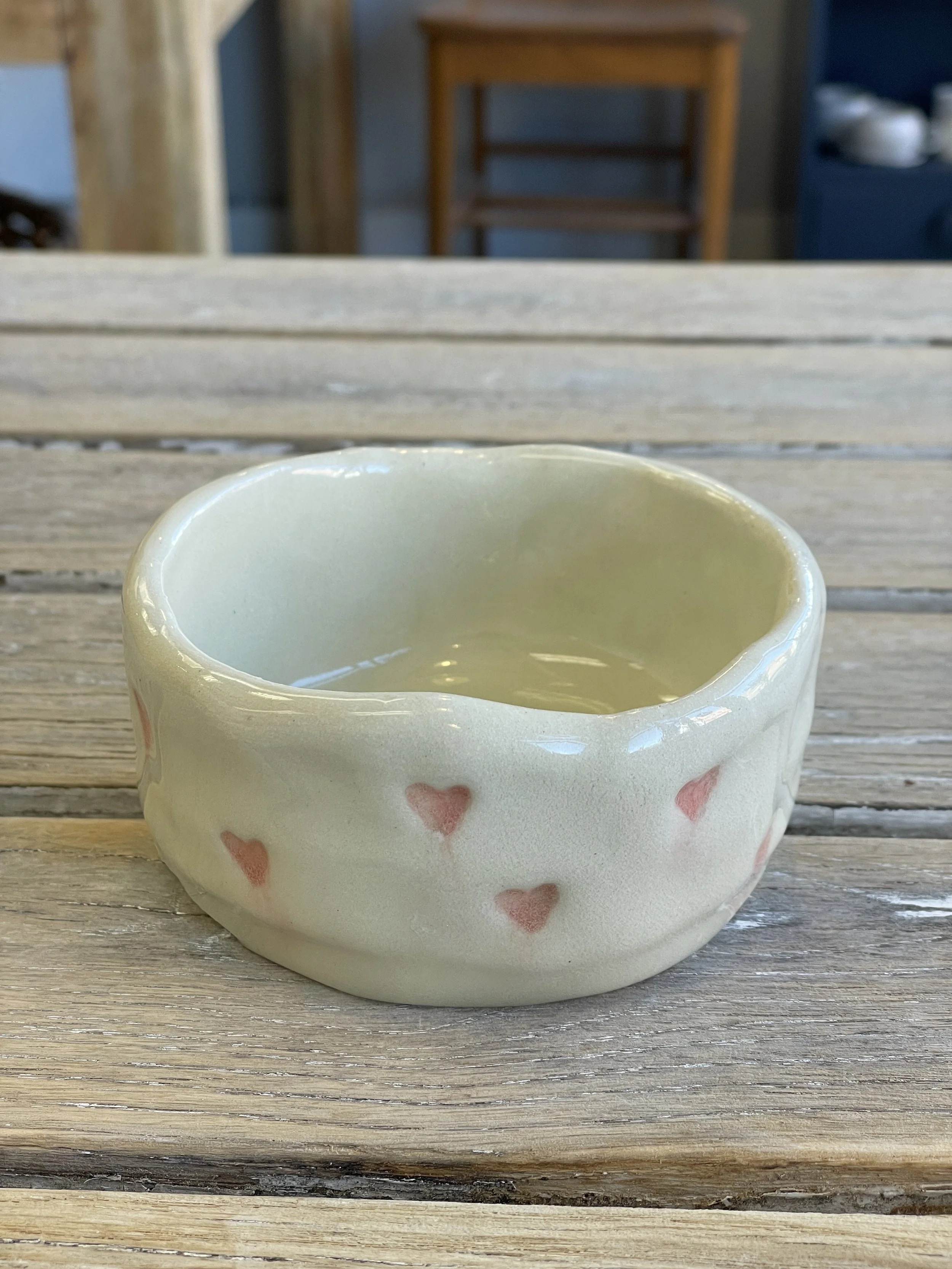 A handmade ceramic bowl with small red heart patterns, placed on a wooden table.