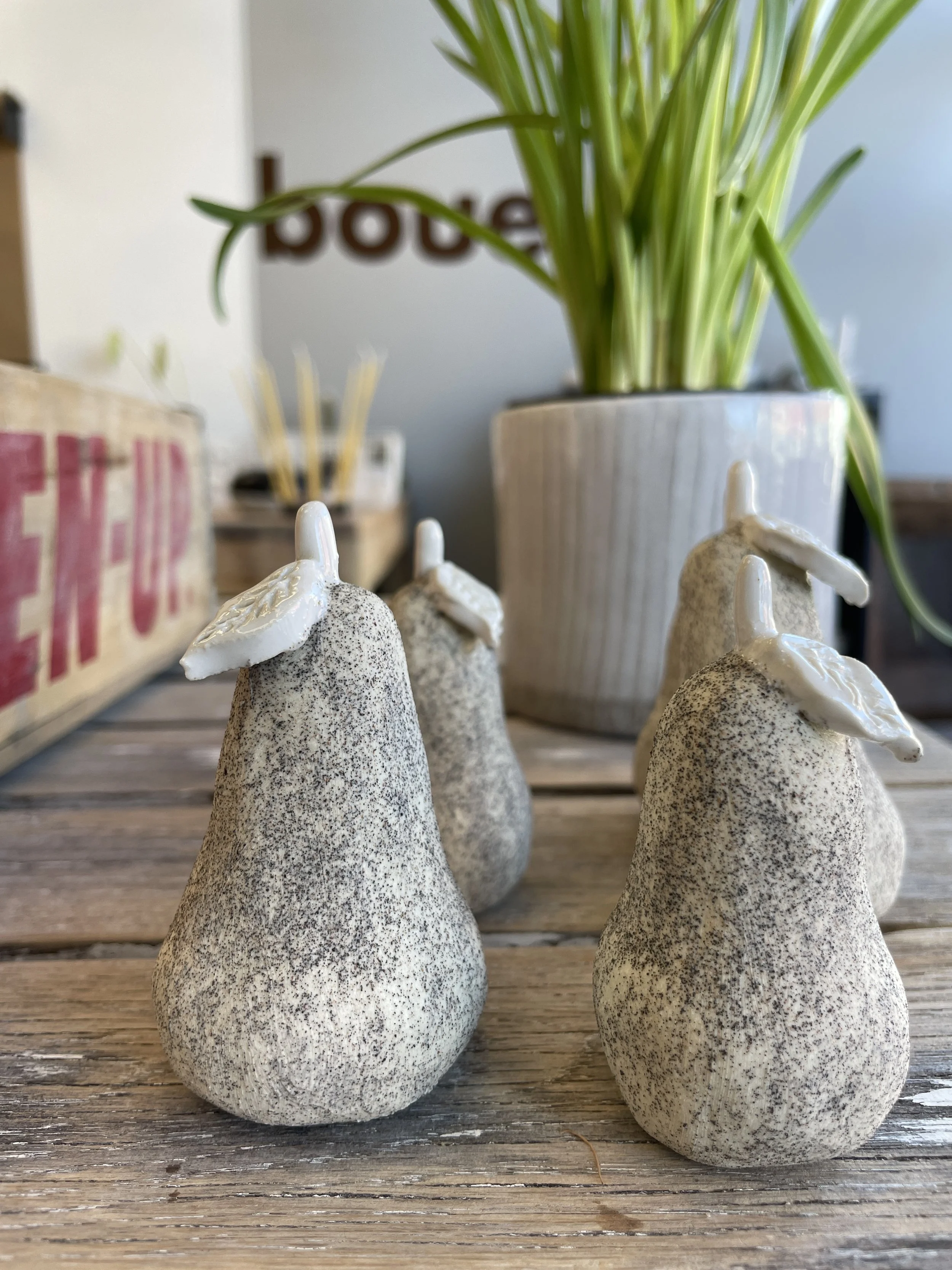 Stone pears with textured surface on wooden table, blurred plant in background.