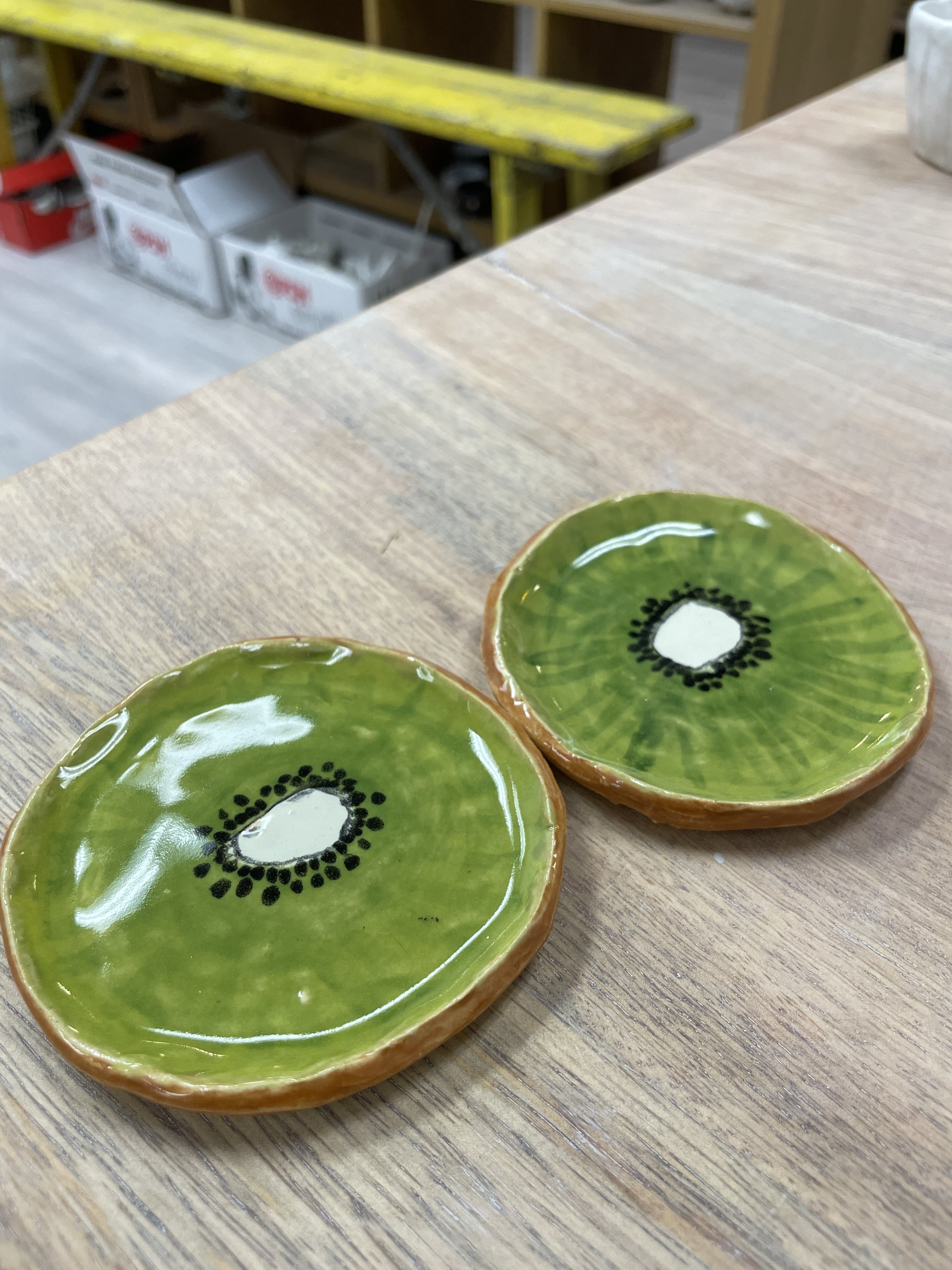 Ceramic coasters designed to look like kiwi slices on a wooden table.
