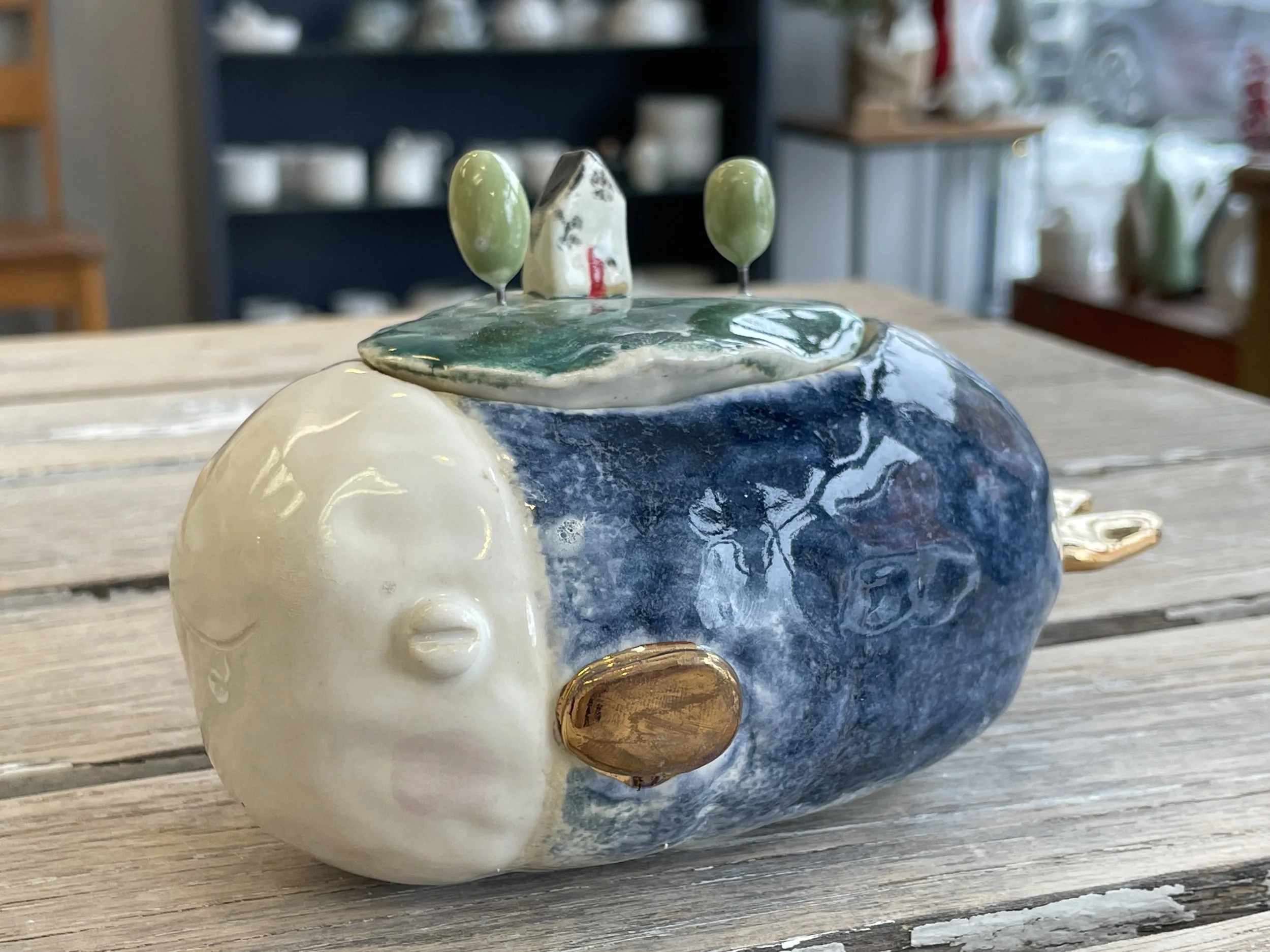 Ceramic whale sculpture with small house and trees on top, placed on a wooden table.