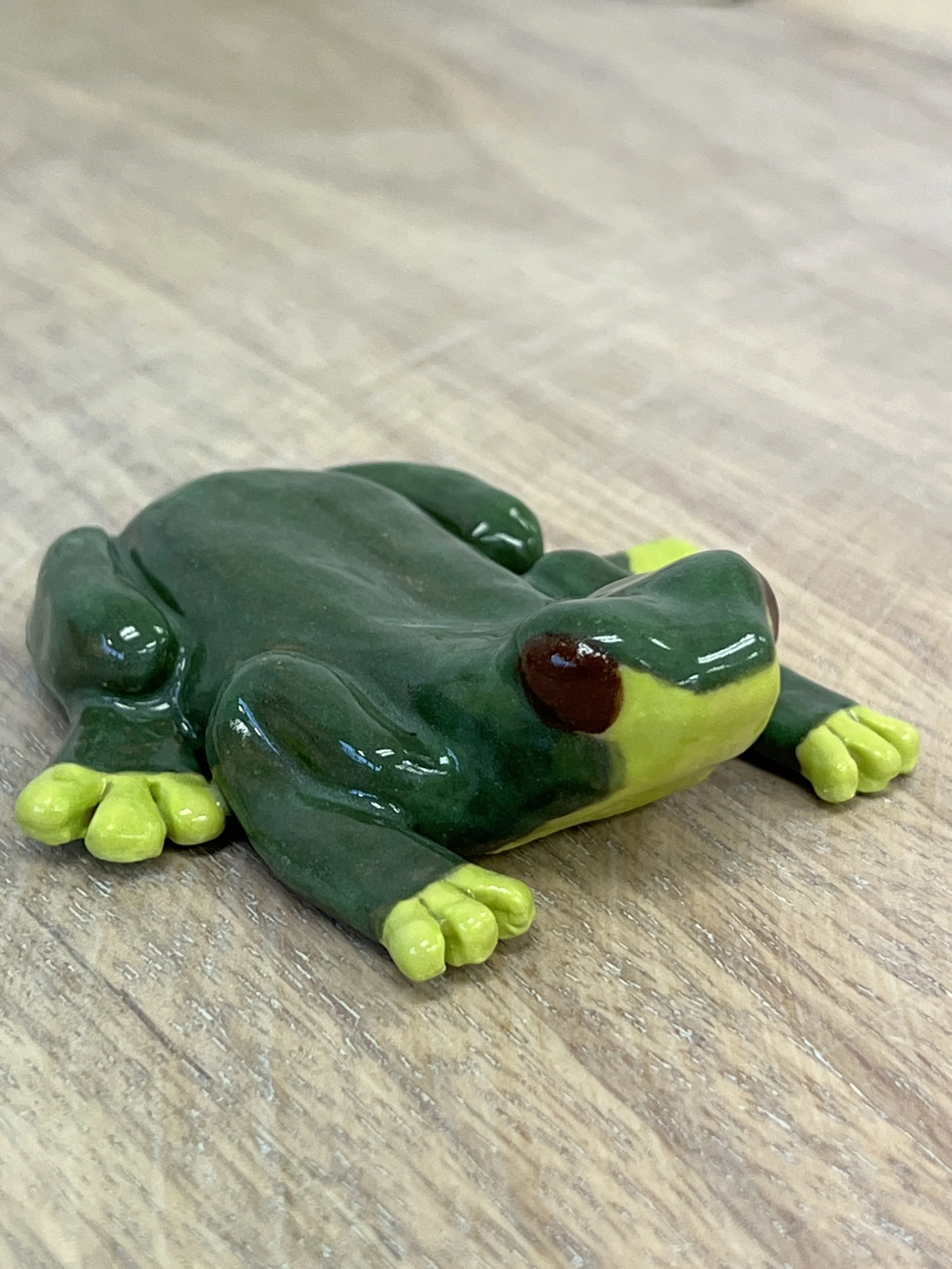 Green ceramic frog figurine on wooden surface