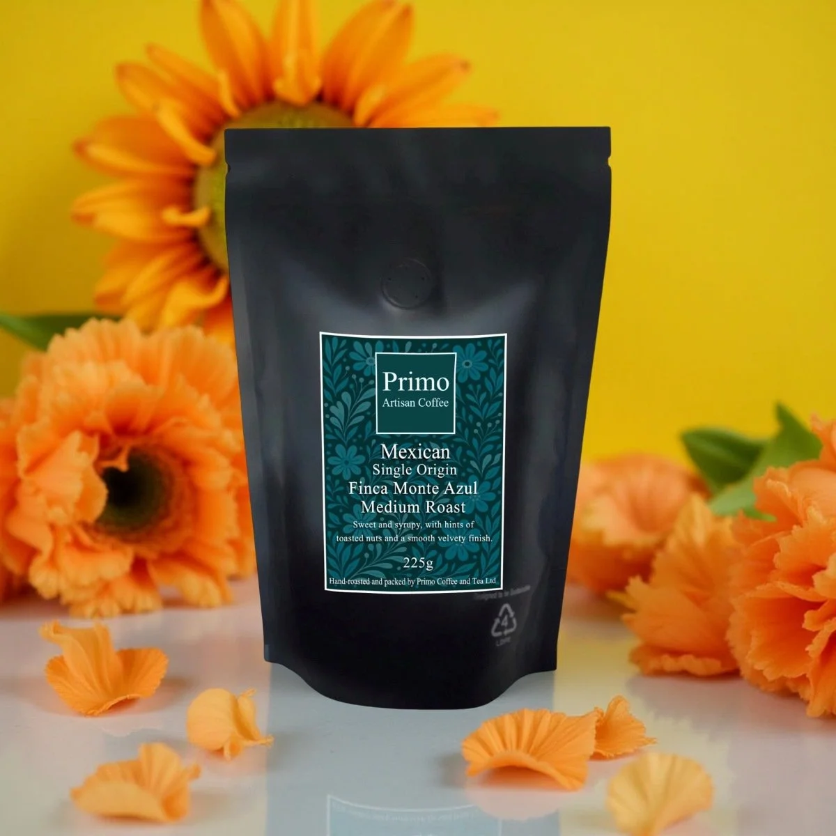 Mexican Single Origin Finca Monte Azul Coffee 225g black bag on a shiny white surface surrounded with orange poppy petals and sunflowers .jpg