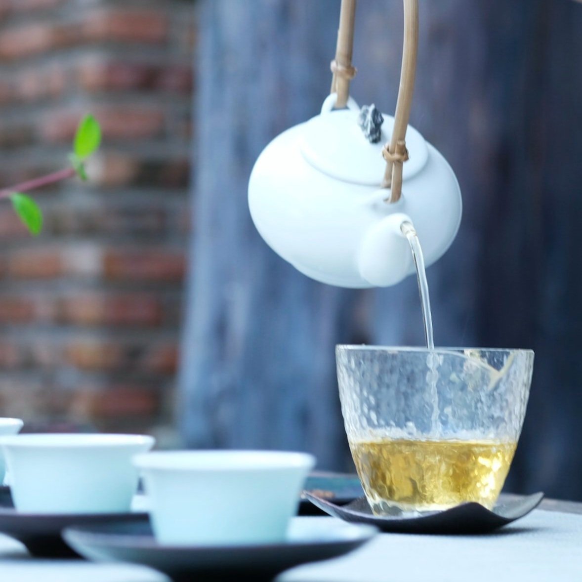 A white china teapot pouring a delicate tea into a glass- primo artisan coffee