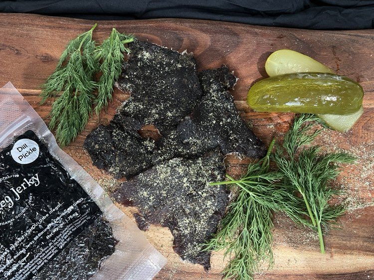 Scrumptious dill pickles and fresh dill hint at the delightful flavor of the dark beef jerky spotlighted in this photo.