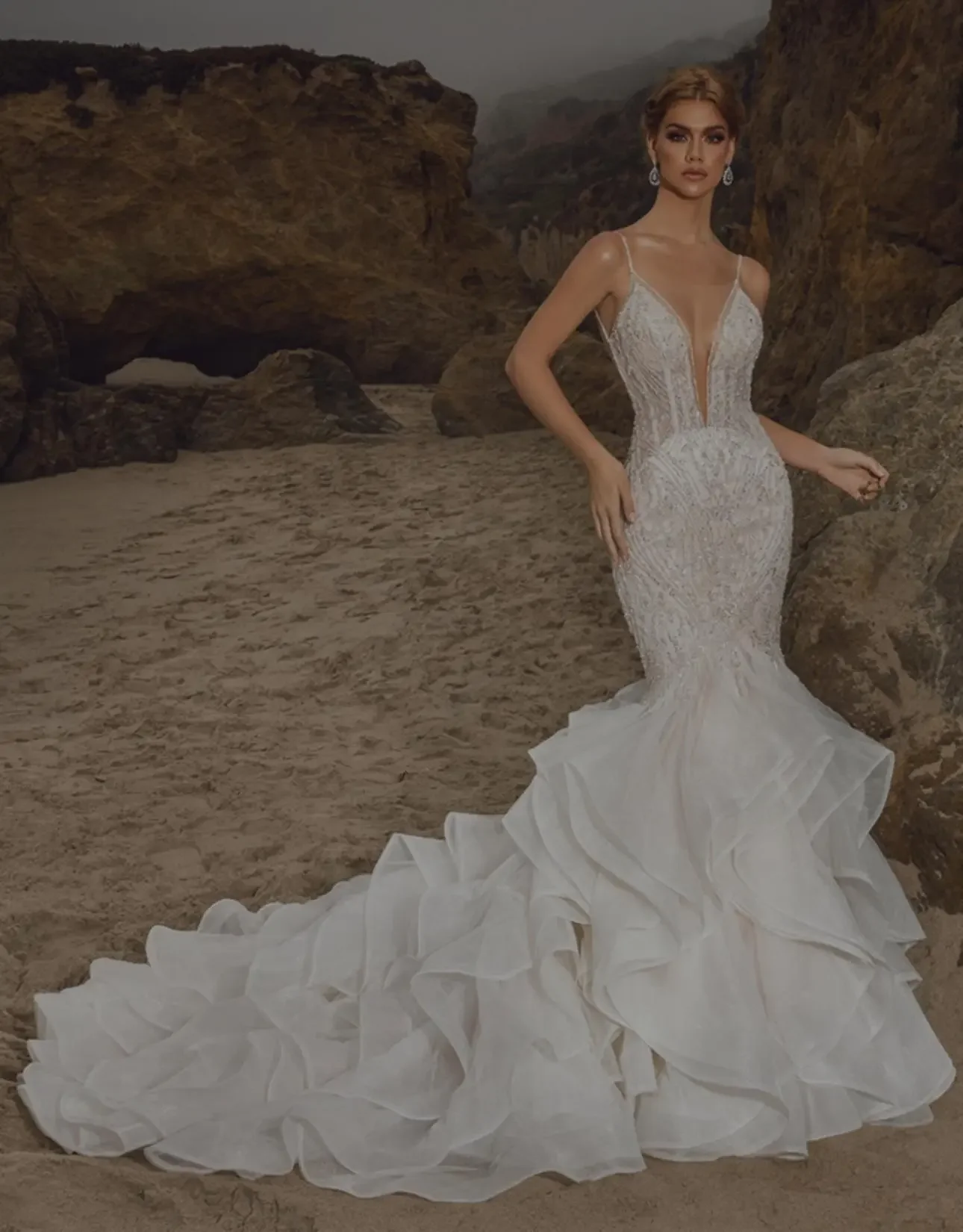 Bride wearing a beaded mermaid wedding dress with deep V neckline and layered train on the beach