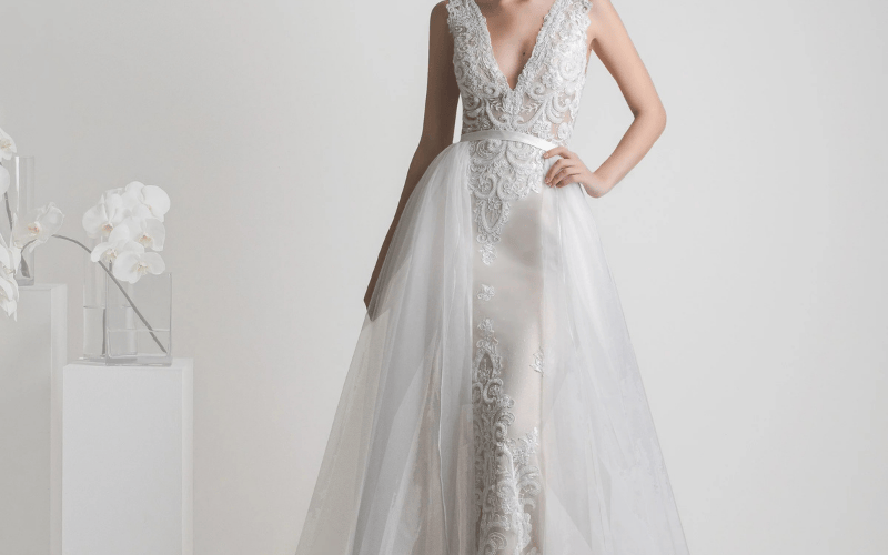 Lace wedding dress with deep V neckline and sheer tulle overskirt reflecting 2026 wedding dress trends.