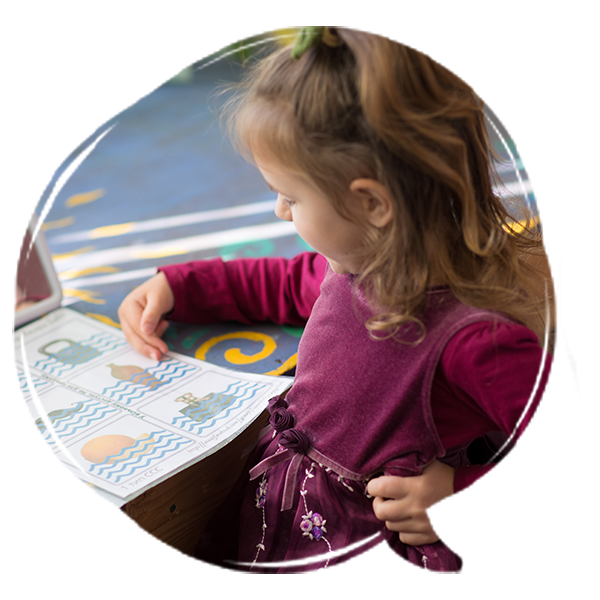 Young girl looking at picture cards during a speech therapy activity at a classroom table.