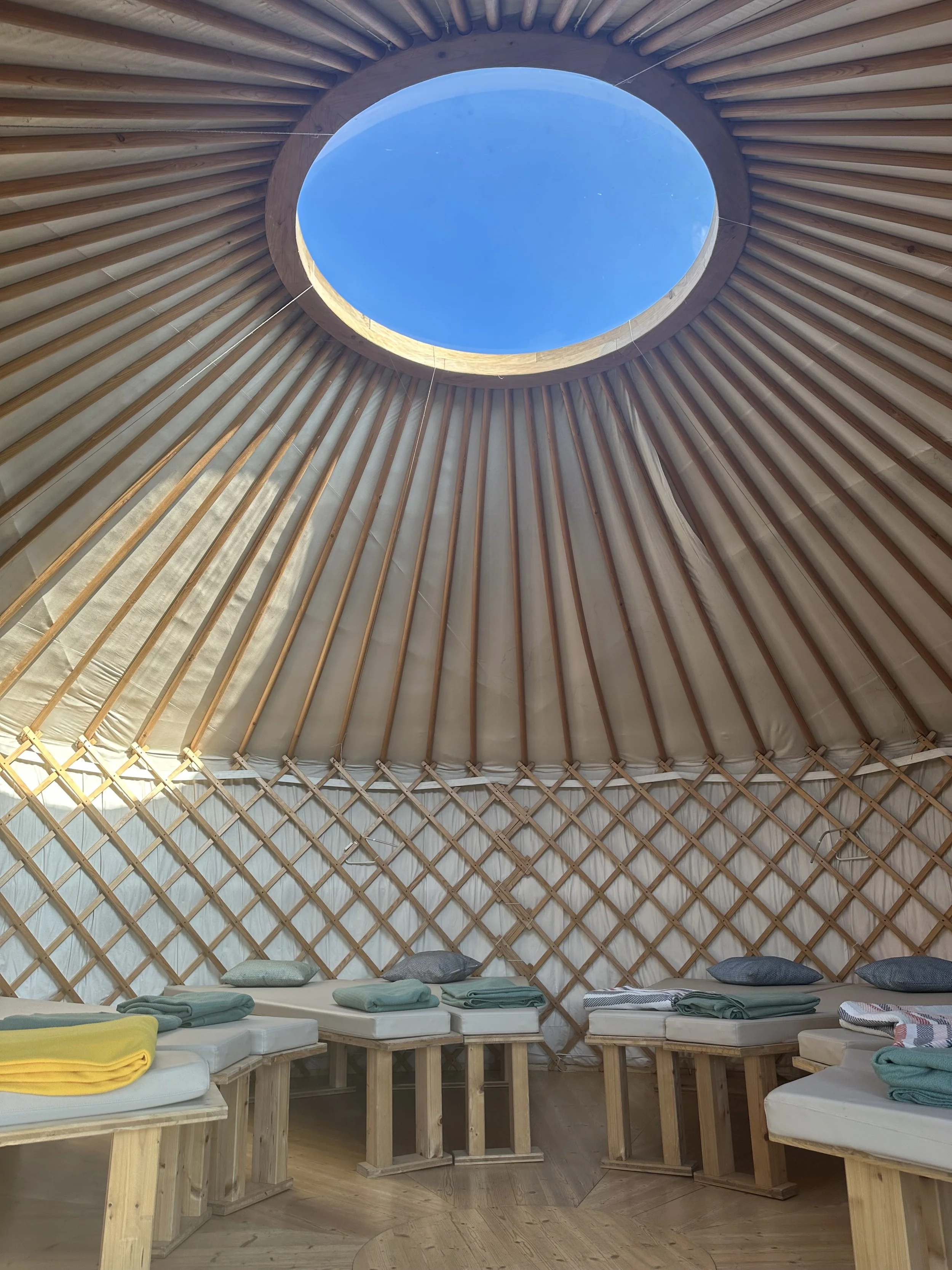 Innenansicht eines zeltähnlichen Raumes mit runden Wänden und einem runden Dachfenster, gefüllt mit Betten und Handtüchern.