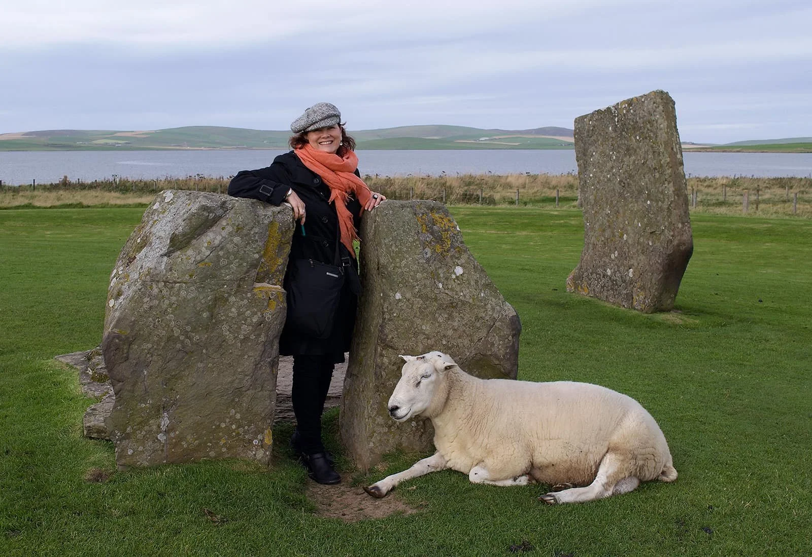 Woman standing amongst Standing Stones with sheep lying in front of stones