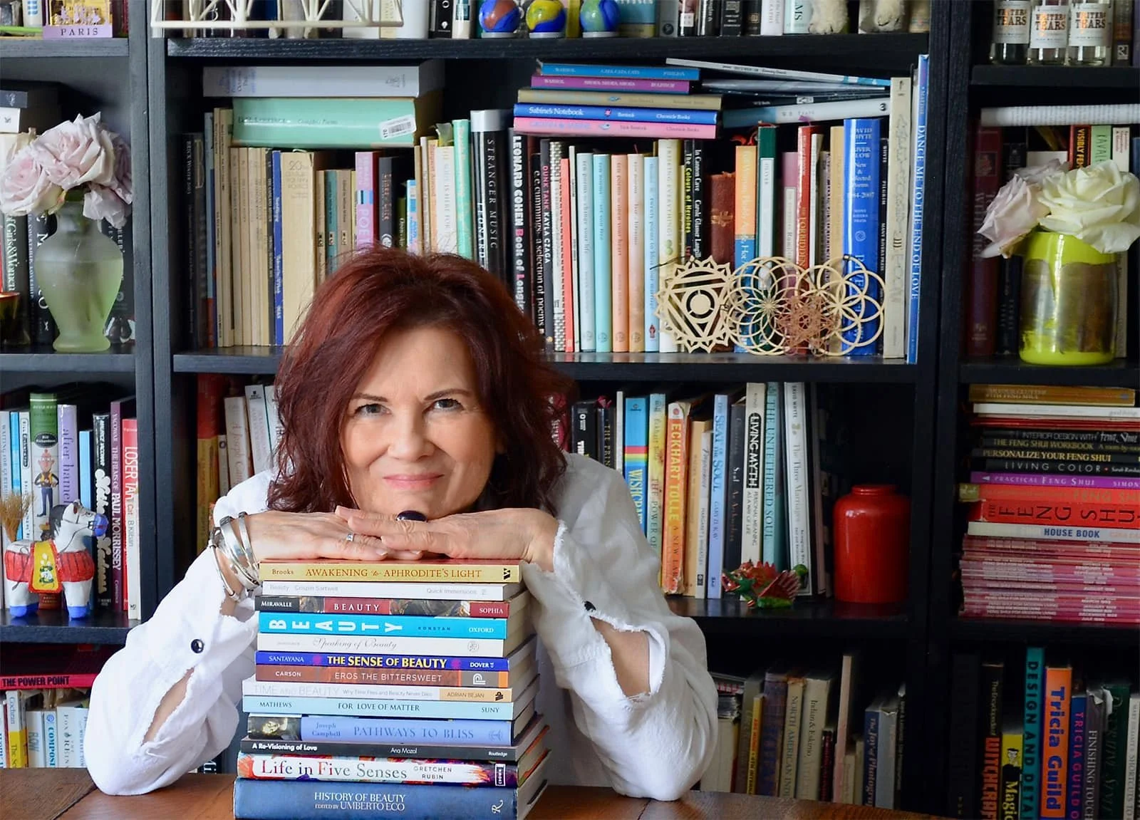 Photo of smiling woman with chin on hands that are placed on top of a stack of books